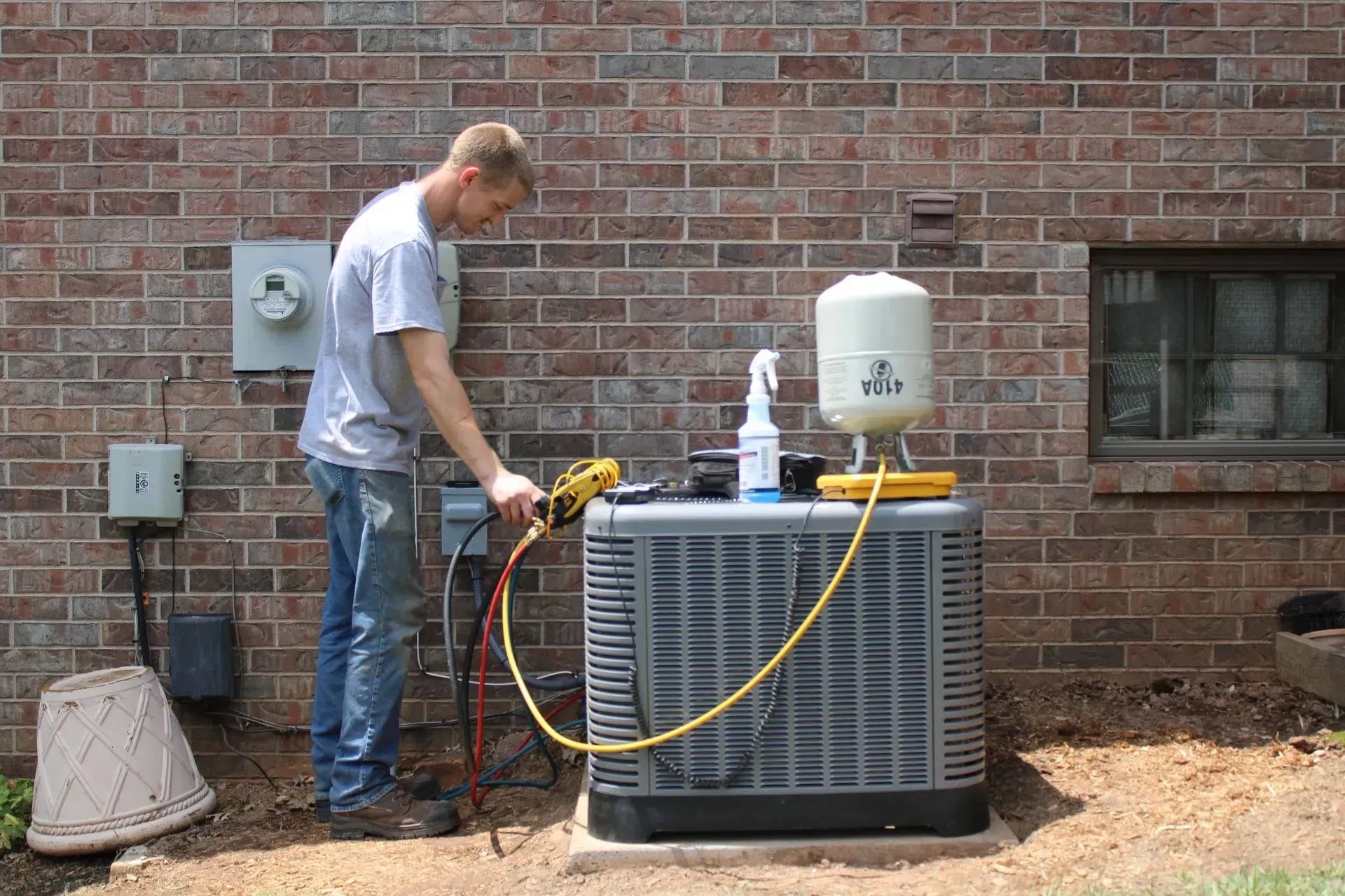 A man is working on an air conditioner outside of a brick building.