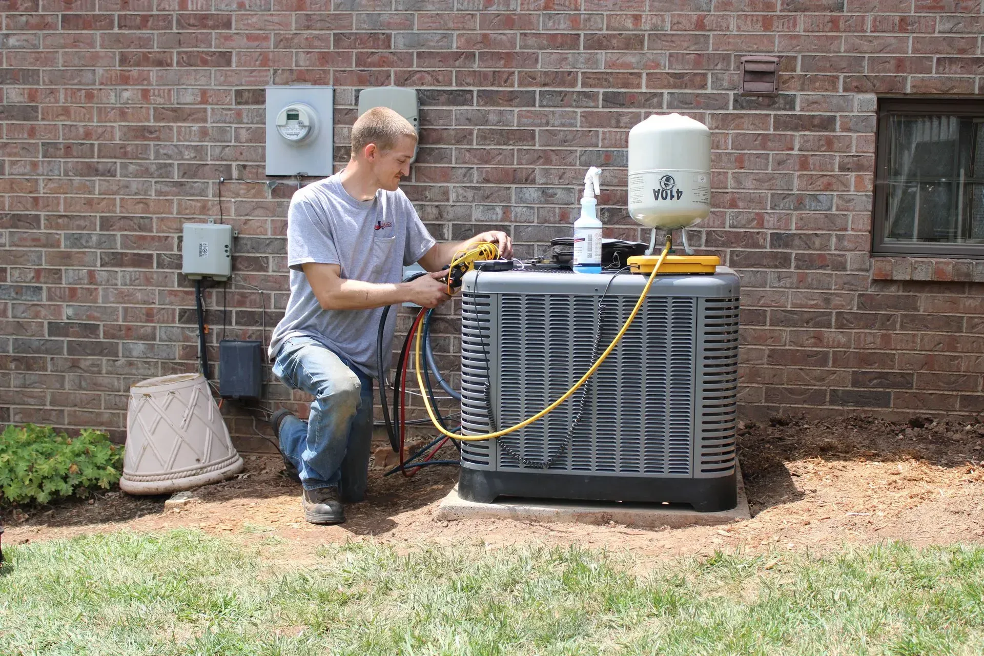 A man is working on an air conditioner outside of a brick building.
