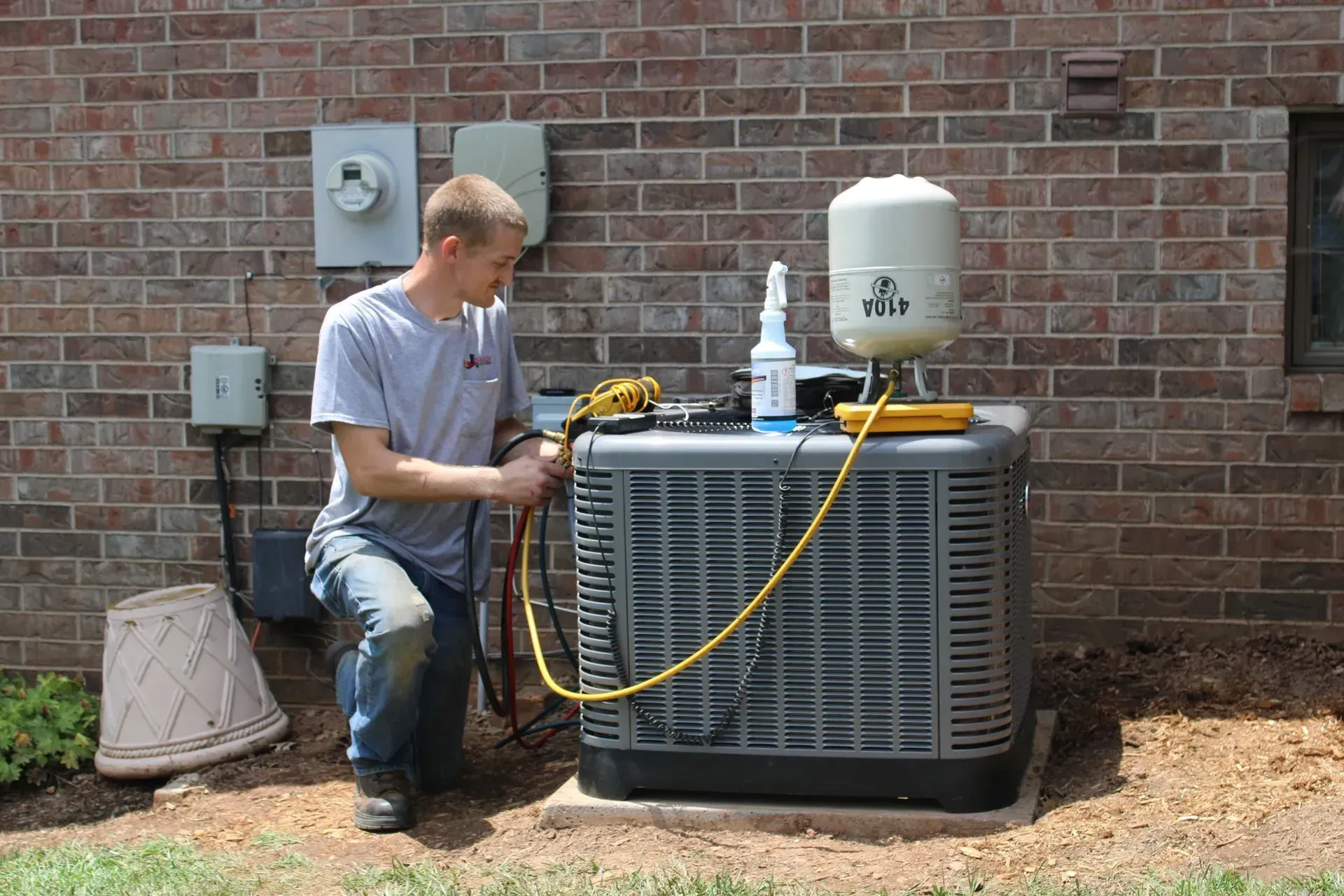 A man is working on an air conditioner outside of a brick building.