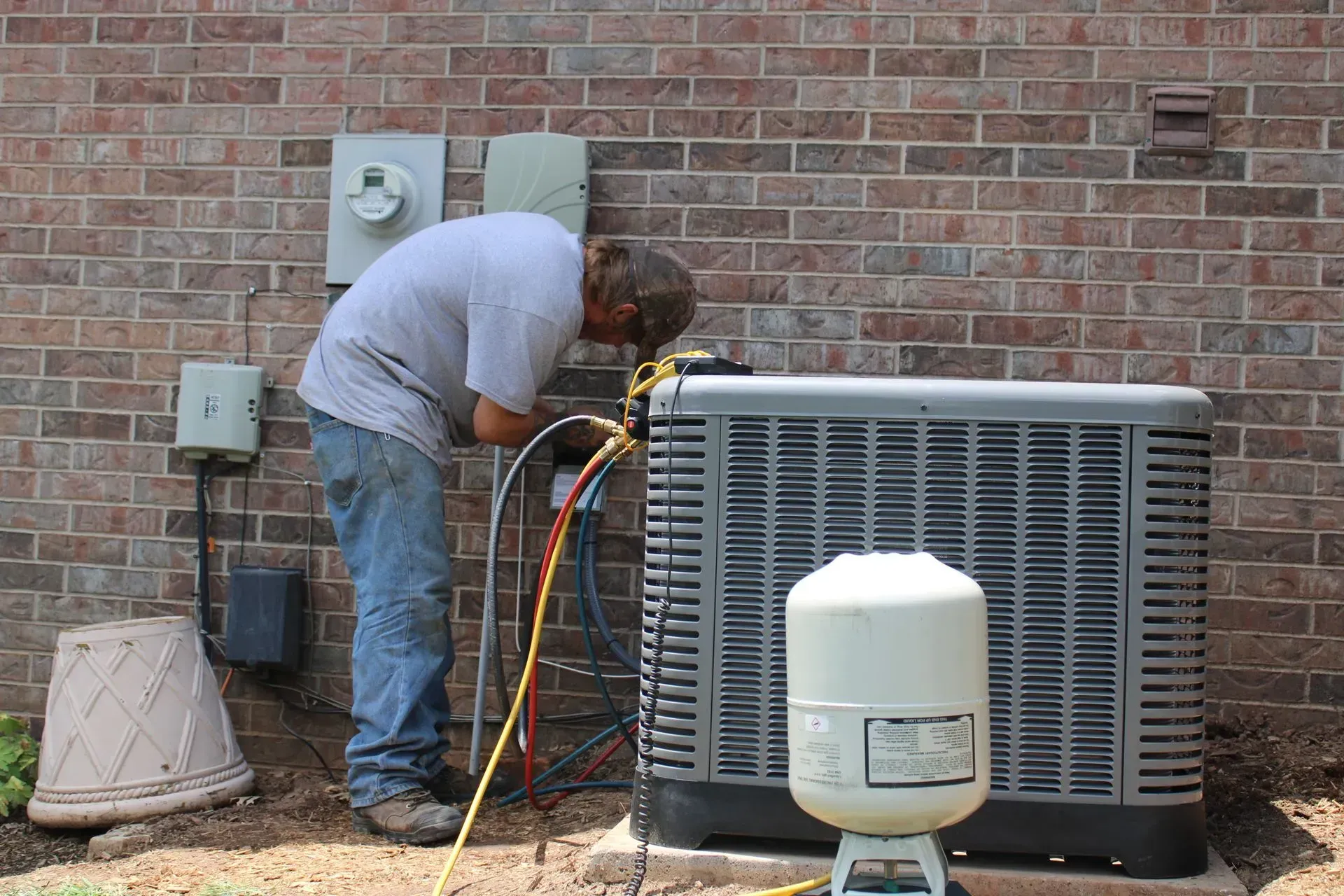 A man is working on an air conditioner outside of a brick building.