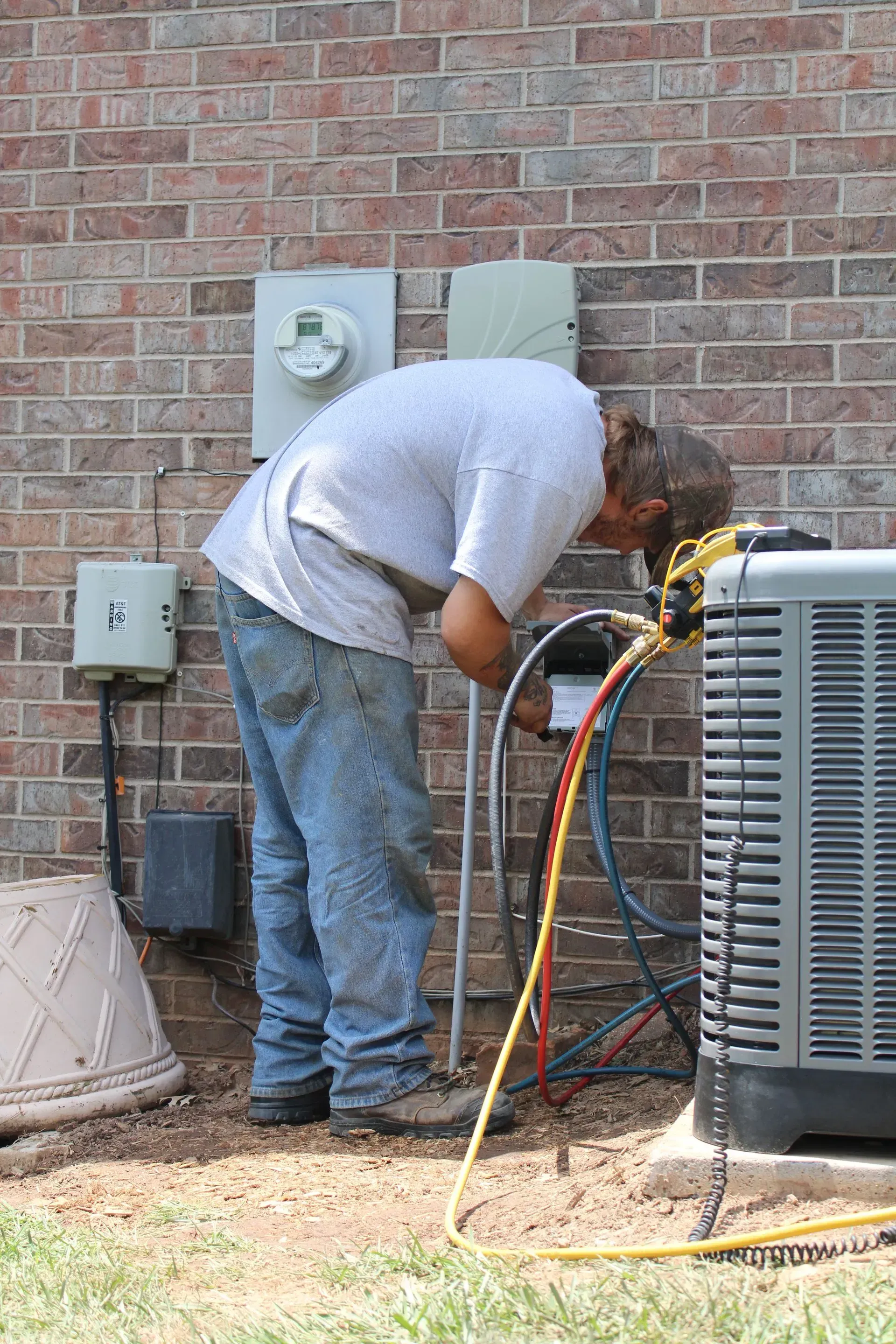 A man is working on an air conditioner outside of a brick building.