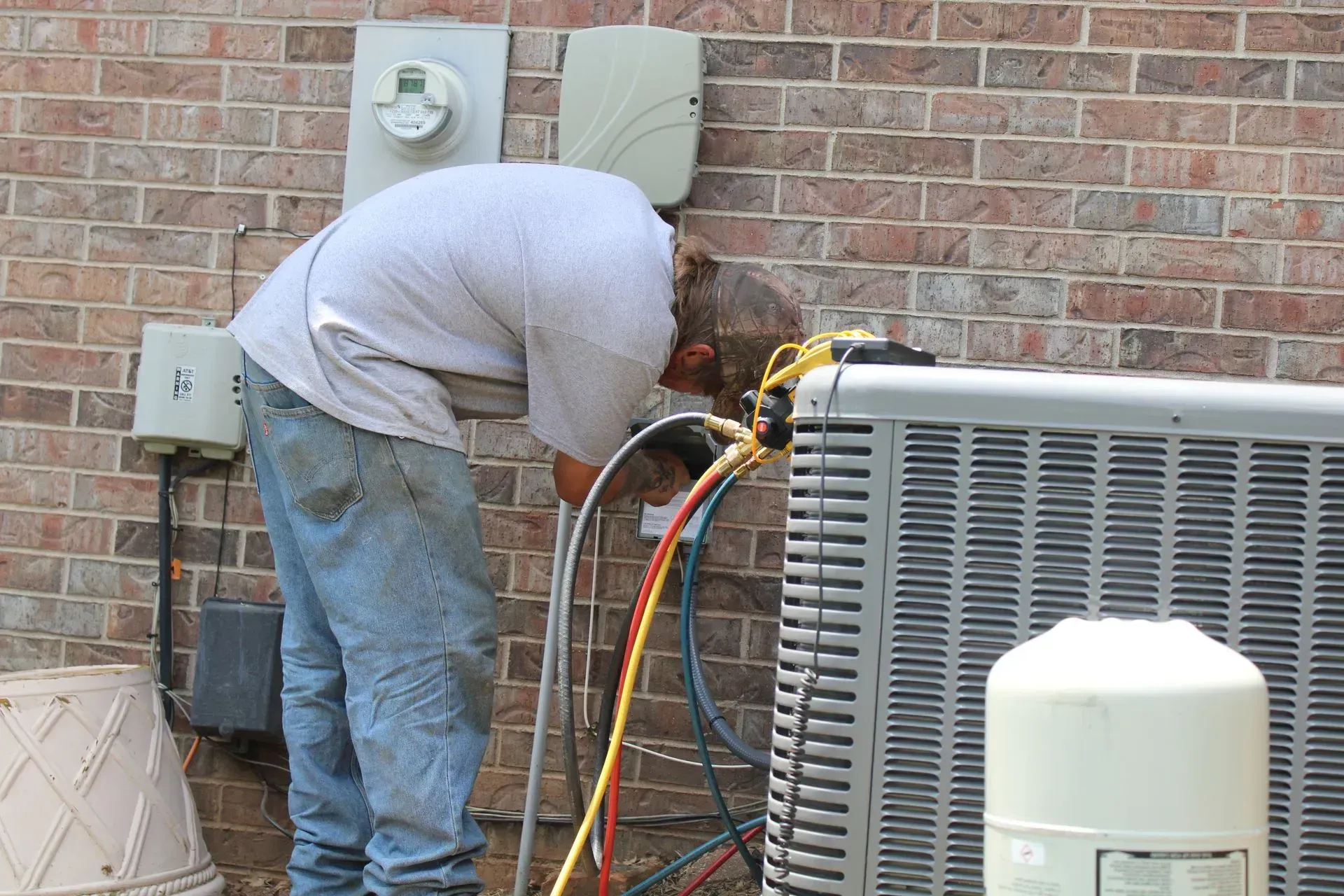 A man is working on an air conditioner outside of a brick building