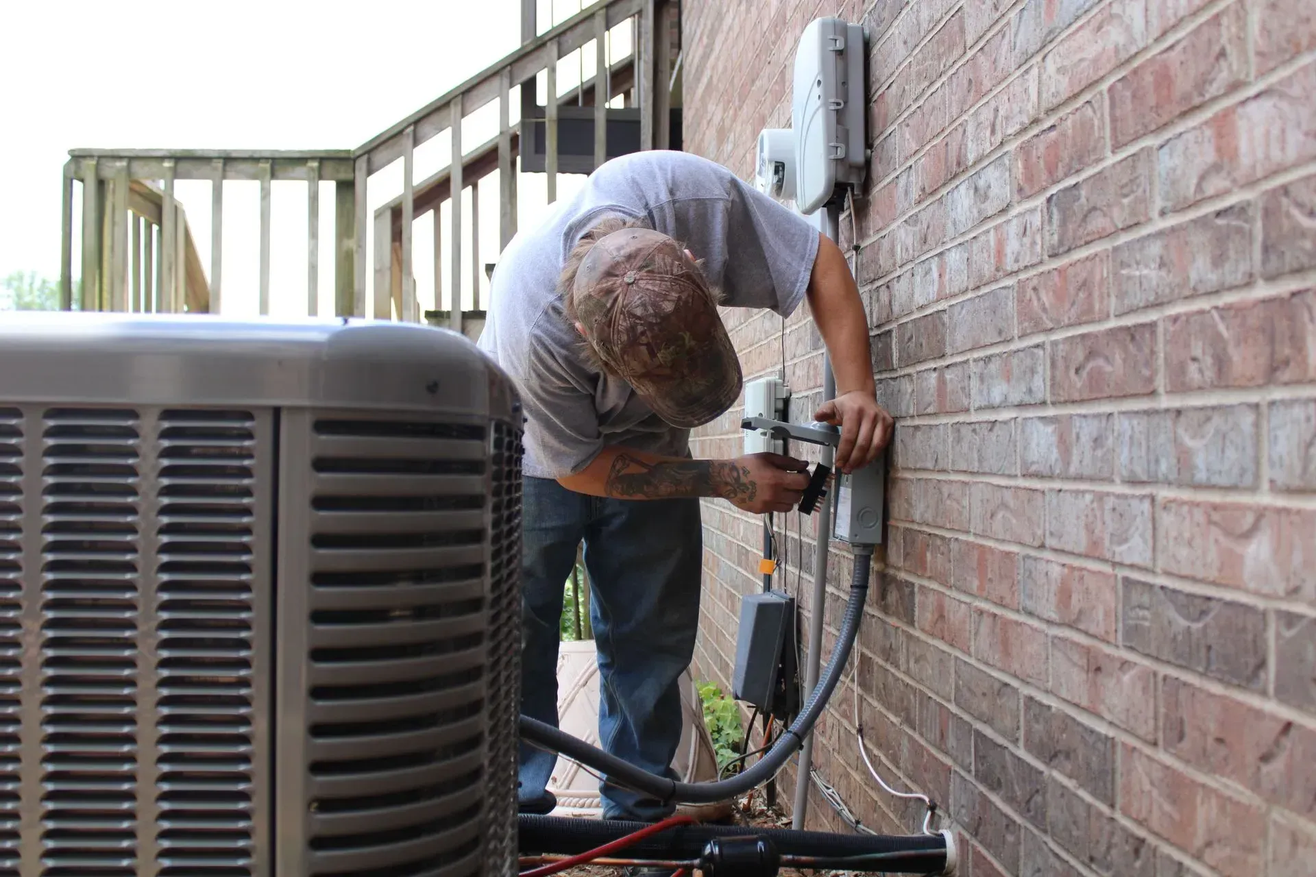 A man is working on an air conditioner on the side of a brick building.
