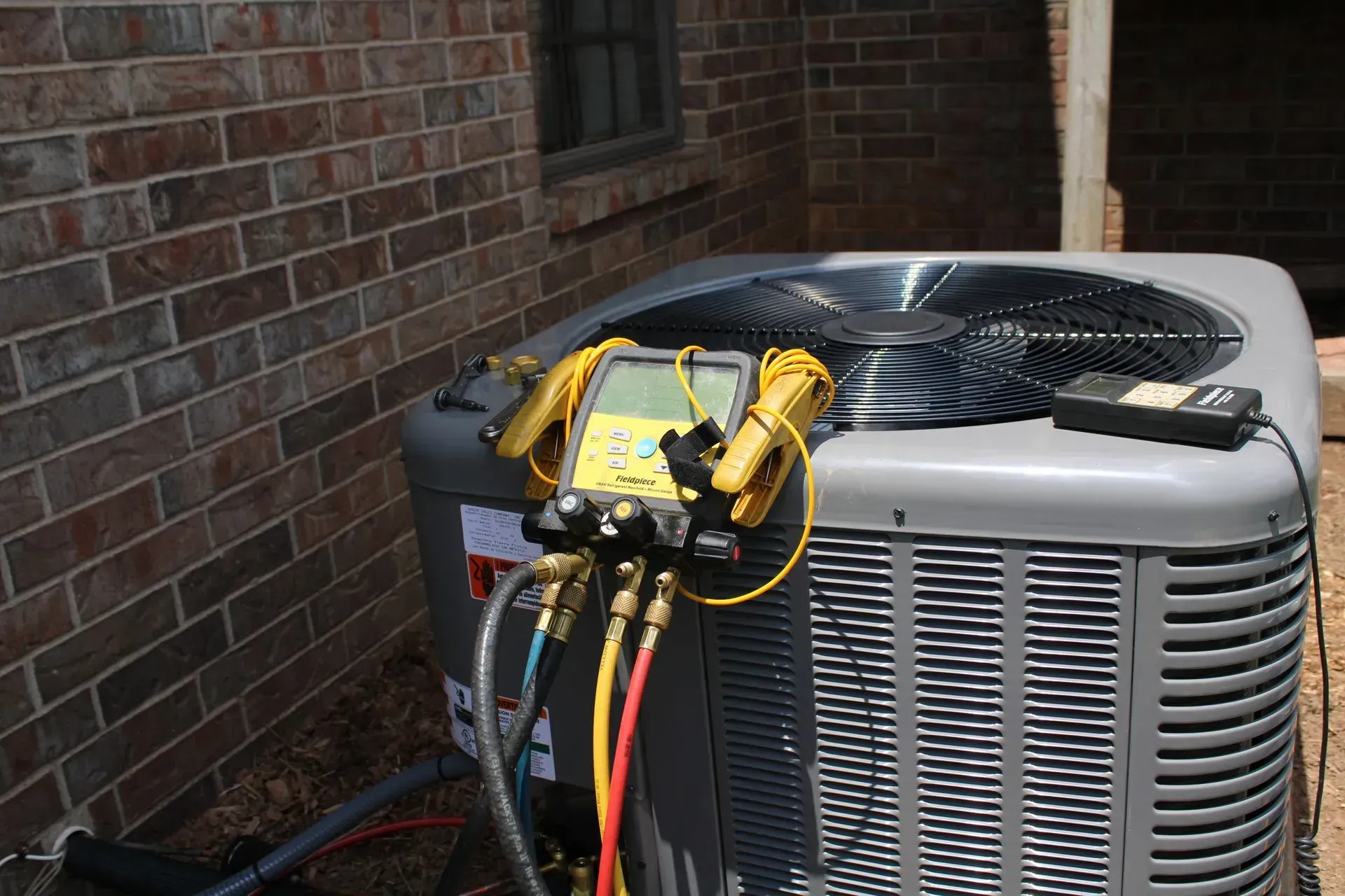 An air conditioner is being serviced outside of a brick building.