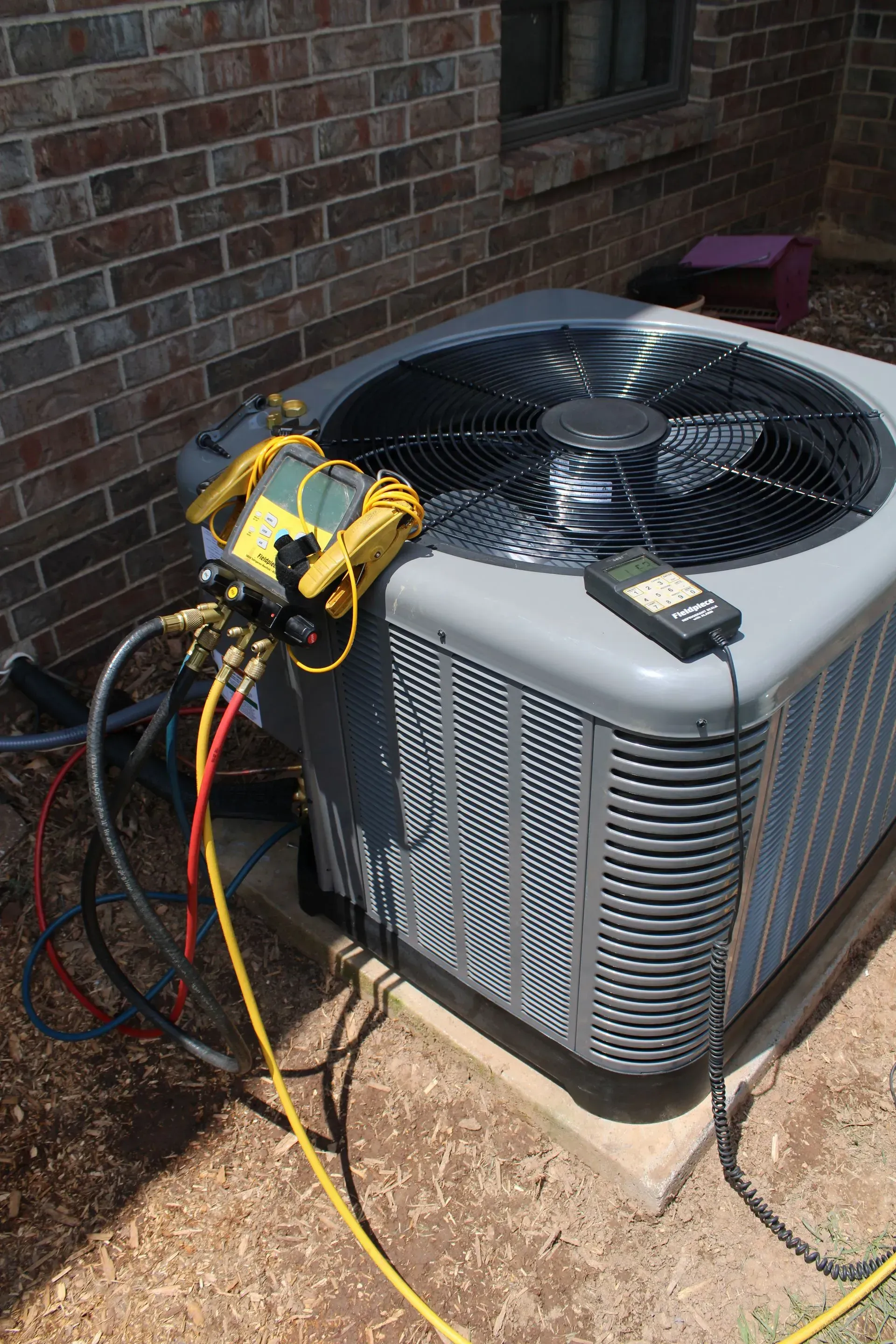 An air conditioner is being serviced outside of a brick building.