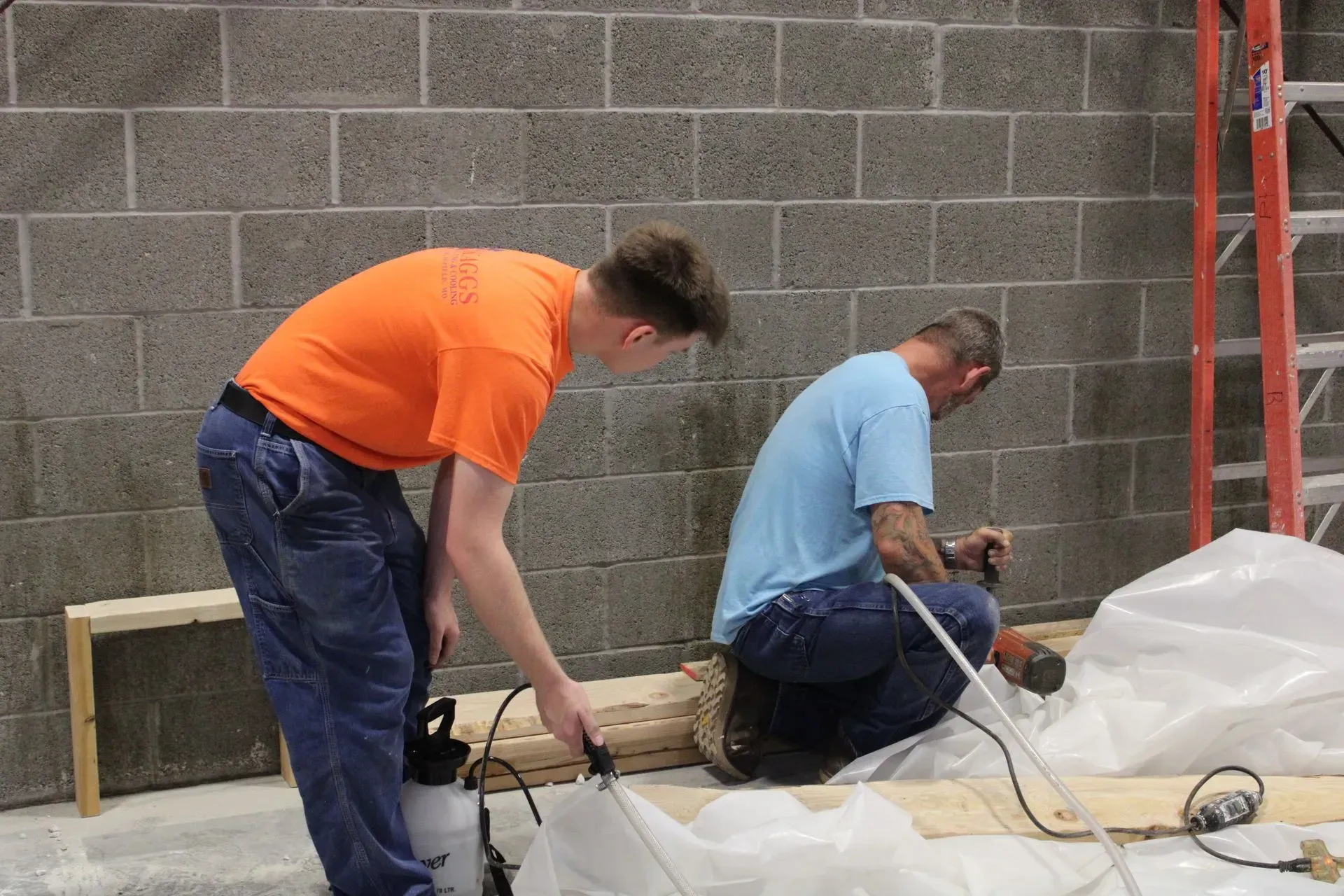 Two men are working on a project in a room with a ladder.