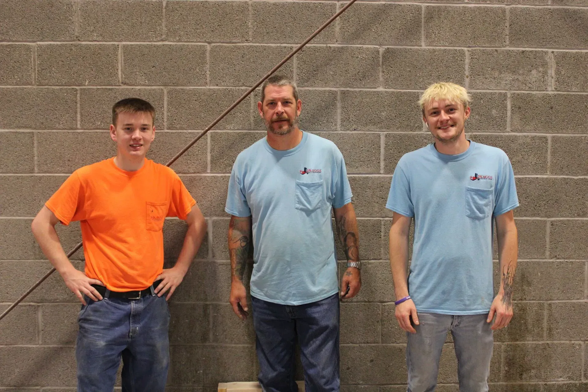 Three men are standing next to each other in front of a brick wall.