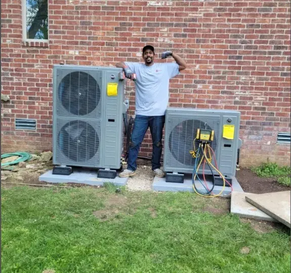 A man is standing next to two air conditioners in front of a brick building.
