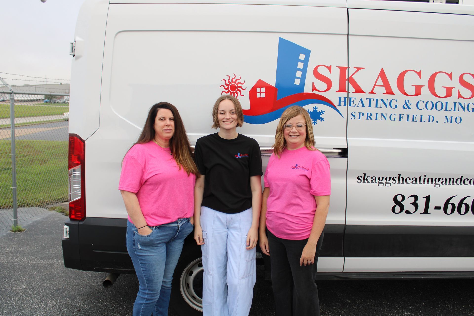 Three women are standing in front of a skaggs heating and cooling van.