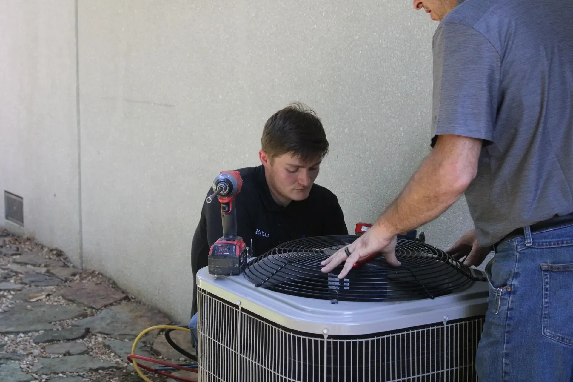 A man is working on an air conditioner while another man looks on.