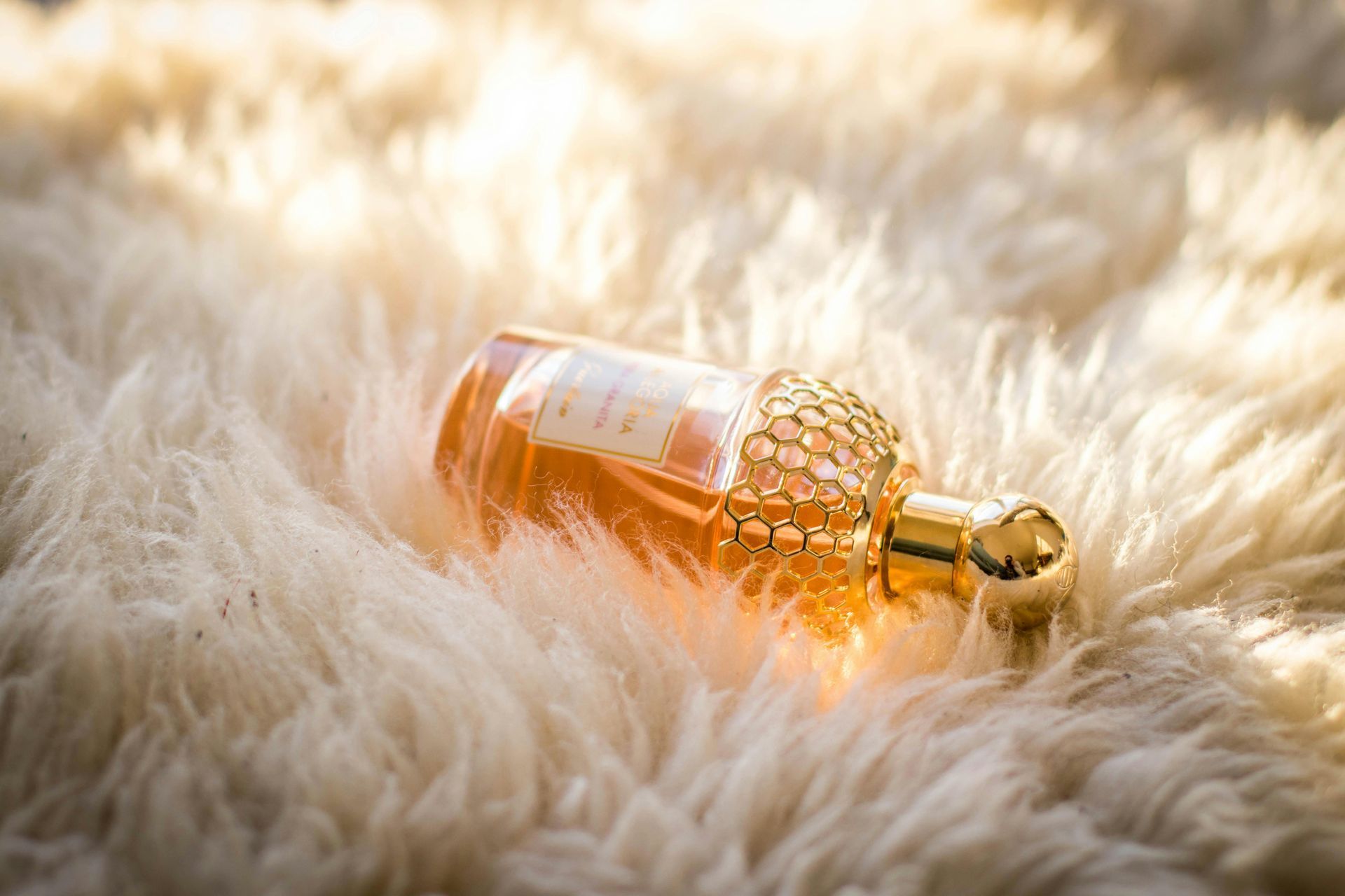 A bottle of perfume is laying on a fluffy blanket.