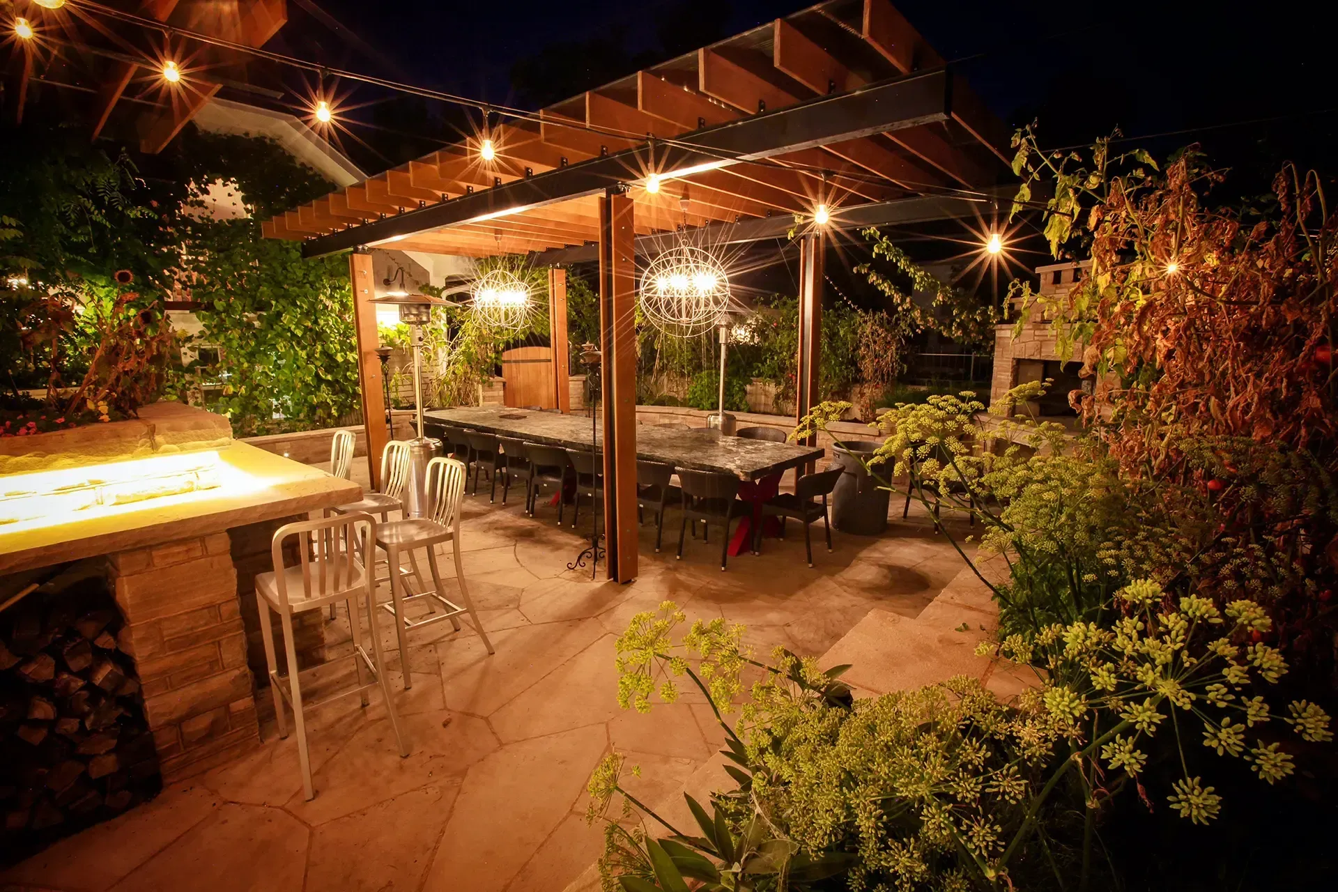 A patio with tables and chairs under a pergola at night
