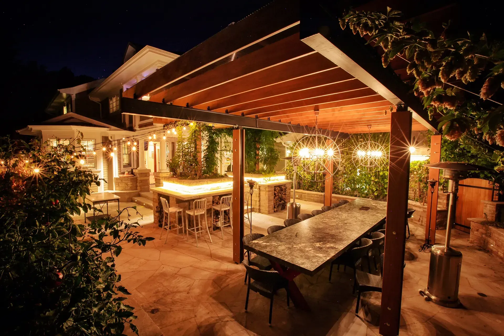 A patio area with a table and chairs under a pergola at night.
