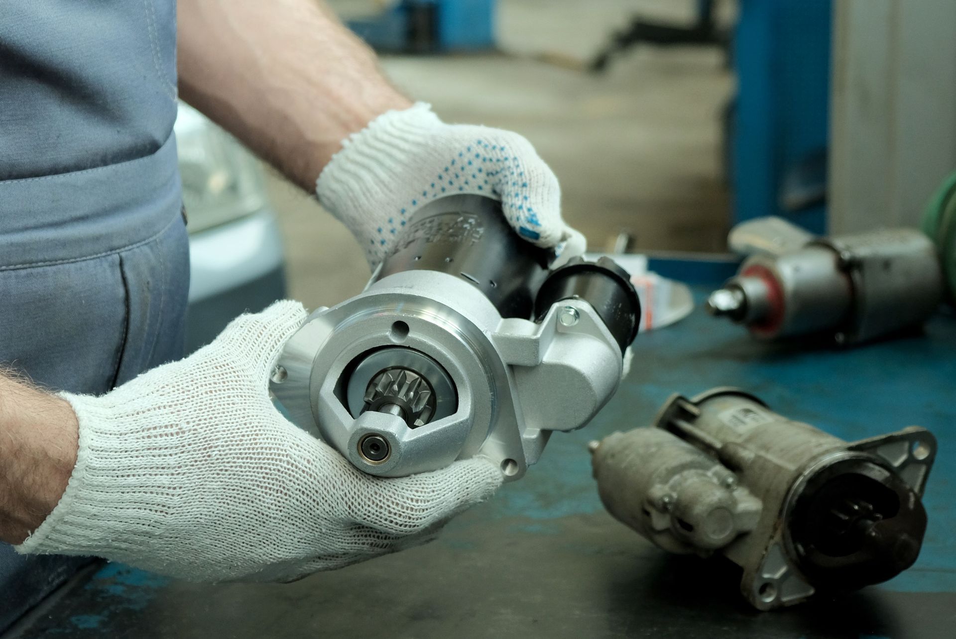 A man is holding a starter in his hands in a garage.