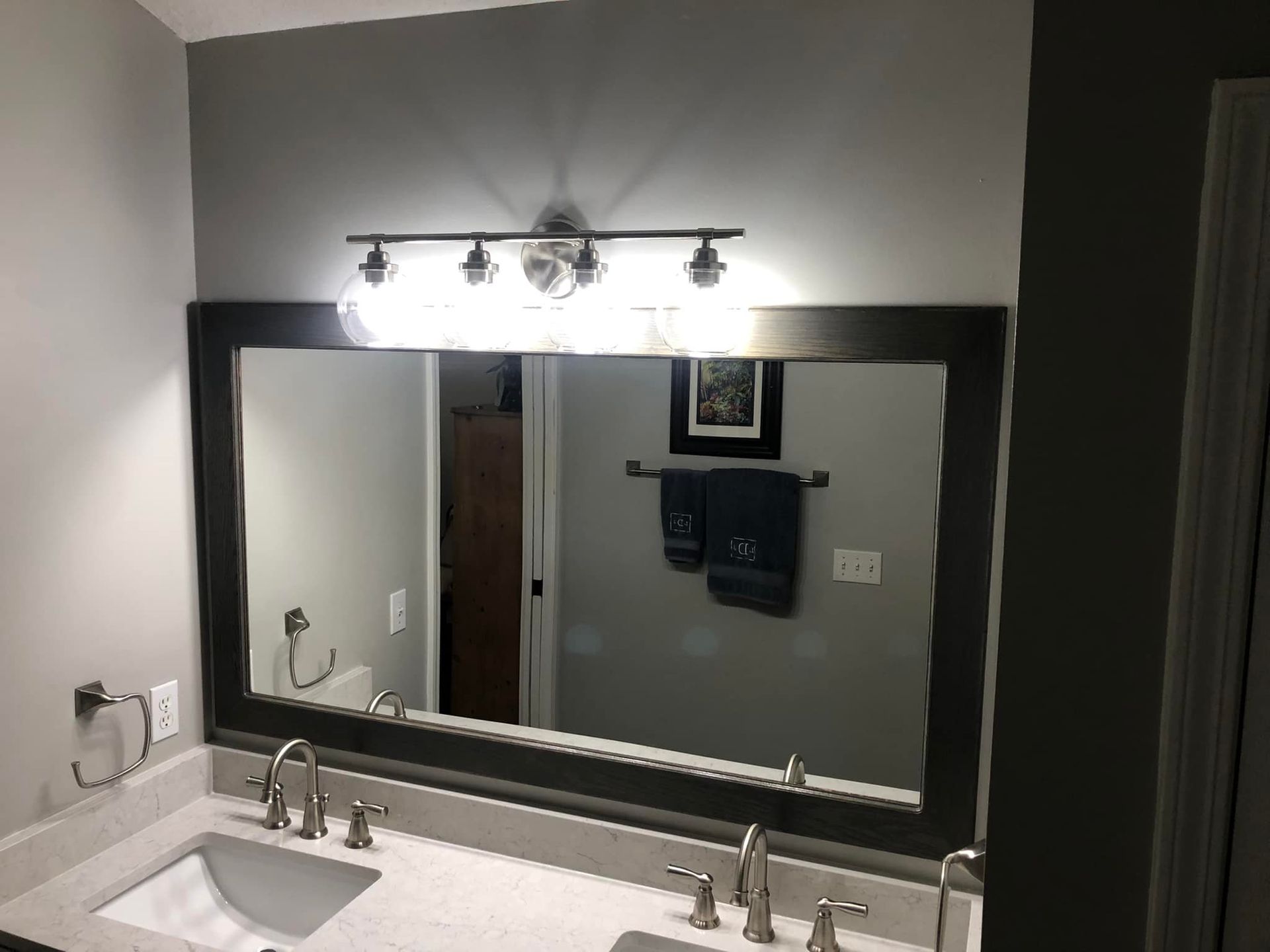 Bathroom with a large mirror framed in dark wood, double sinks, and a light fixture above.