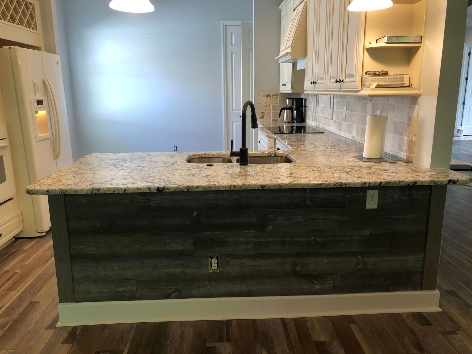 Kitchen island with gray granite countertop, wood paneling, and sink.
