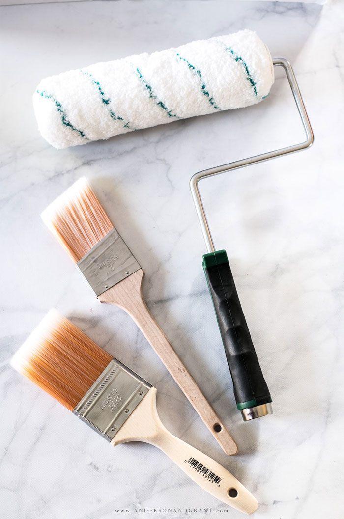 Paint roller and two paint brushes on a light-colored surface.