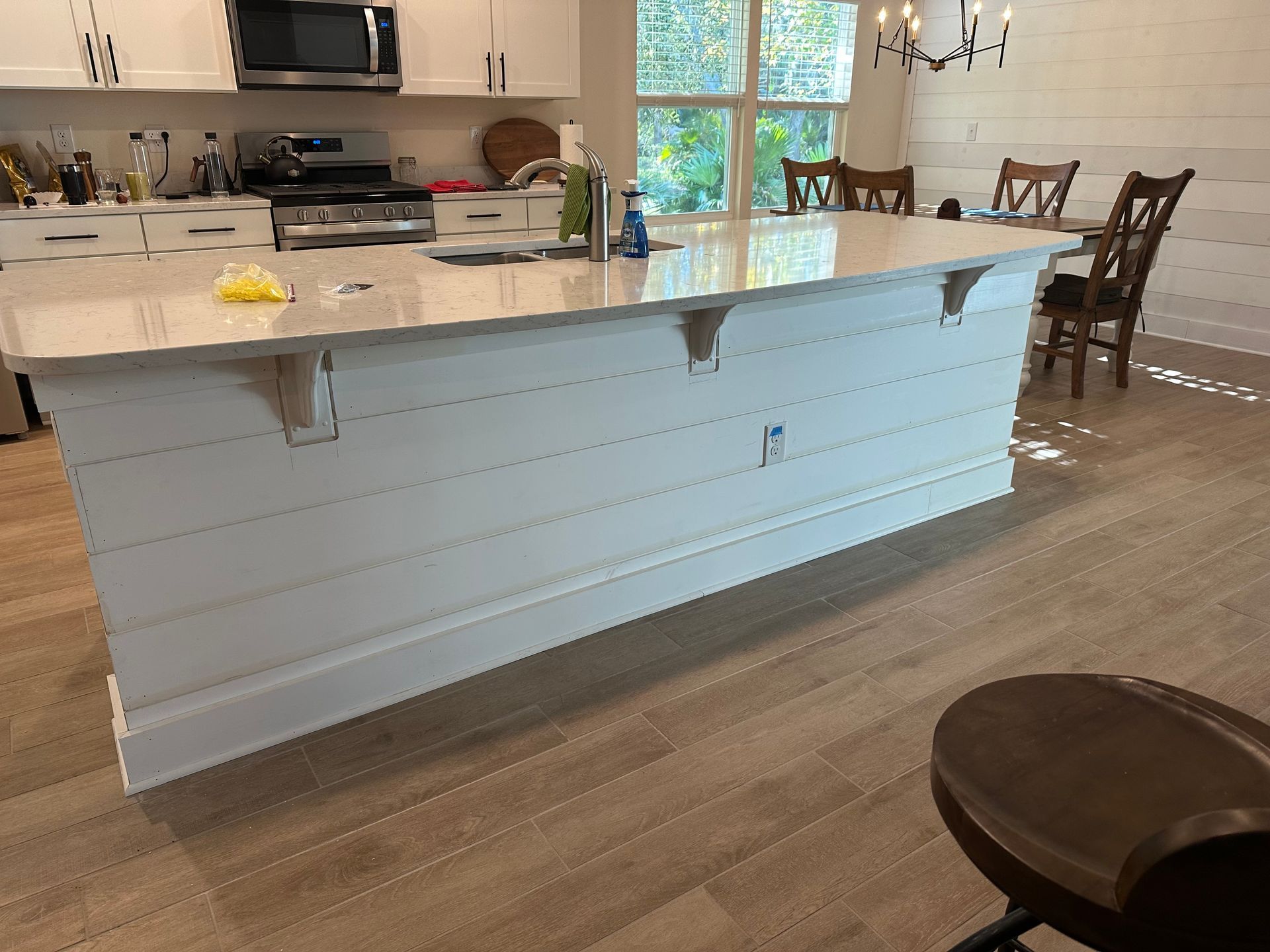 White kitchen island with a light-colored countertop, shiplap siding, and wood floor.