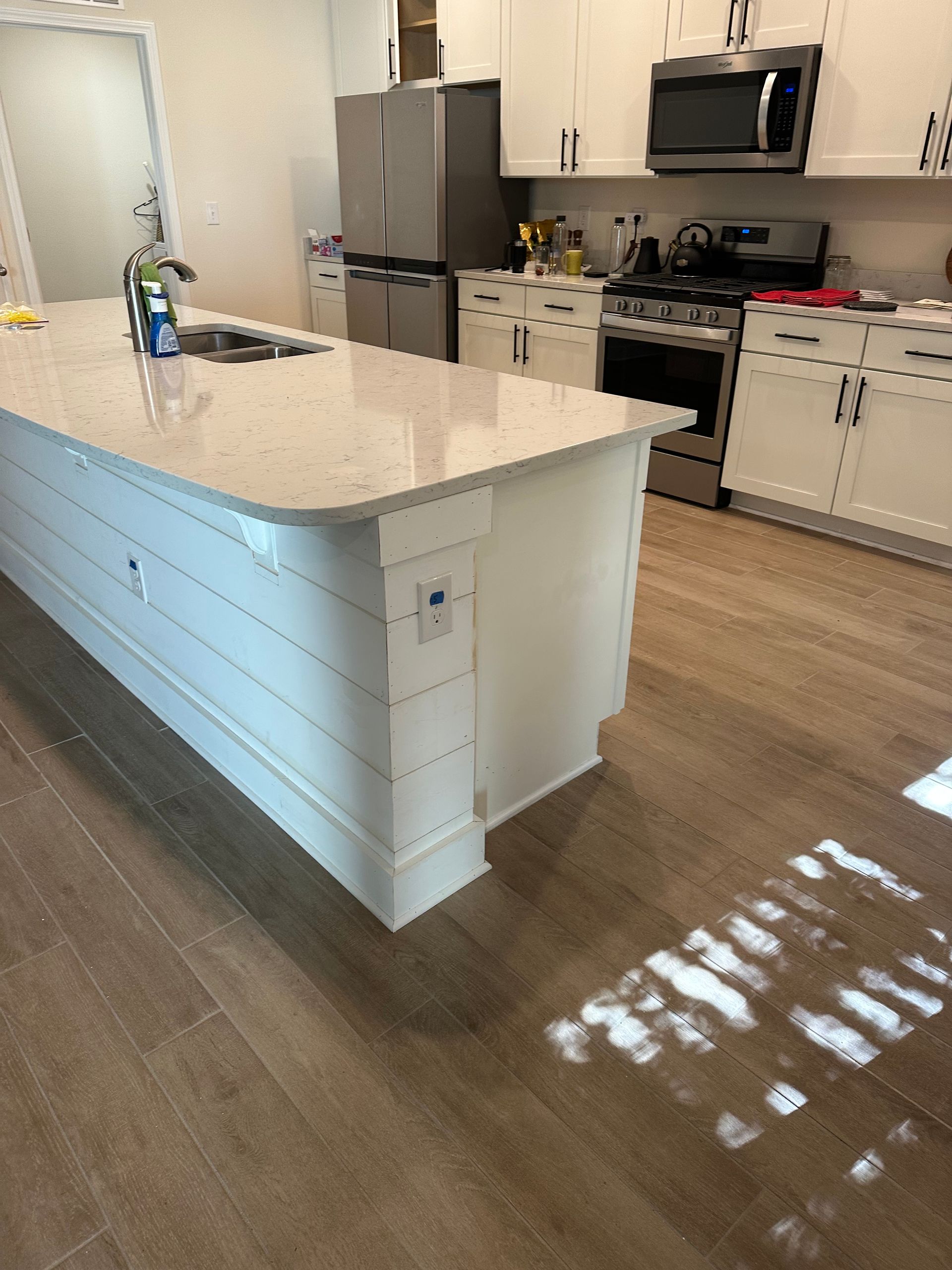 Modern kitchen with a white island, stainless steel appliances, and wood-look flooring.