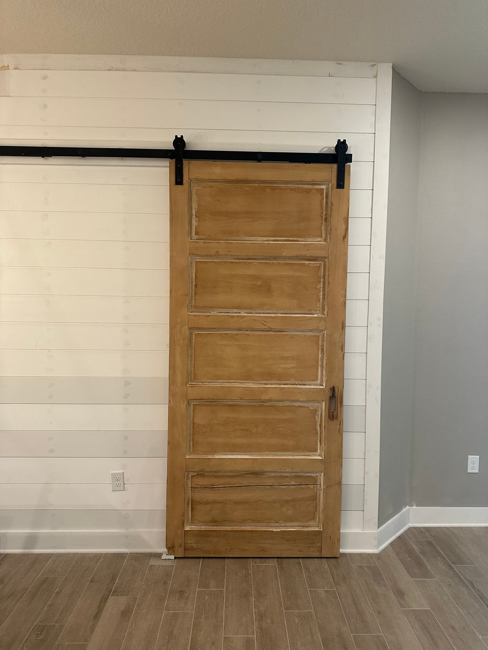 Barn door on a white paneled wall with a black track, installed against a gray wall.