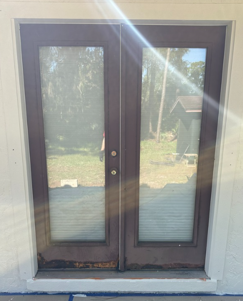 Two brown French doors with glass panes, set in a white frame, with a bright sun flare.