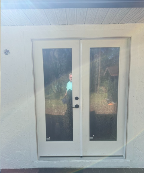 White double doors with glass panels, set in a white frame, with a person reflected in the glass.