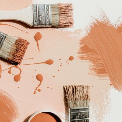 Paintbrushes with orange paint and splotches on a light peach background.