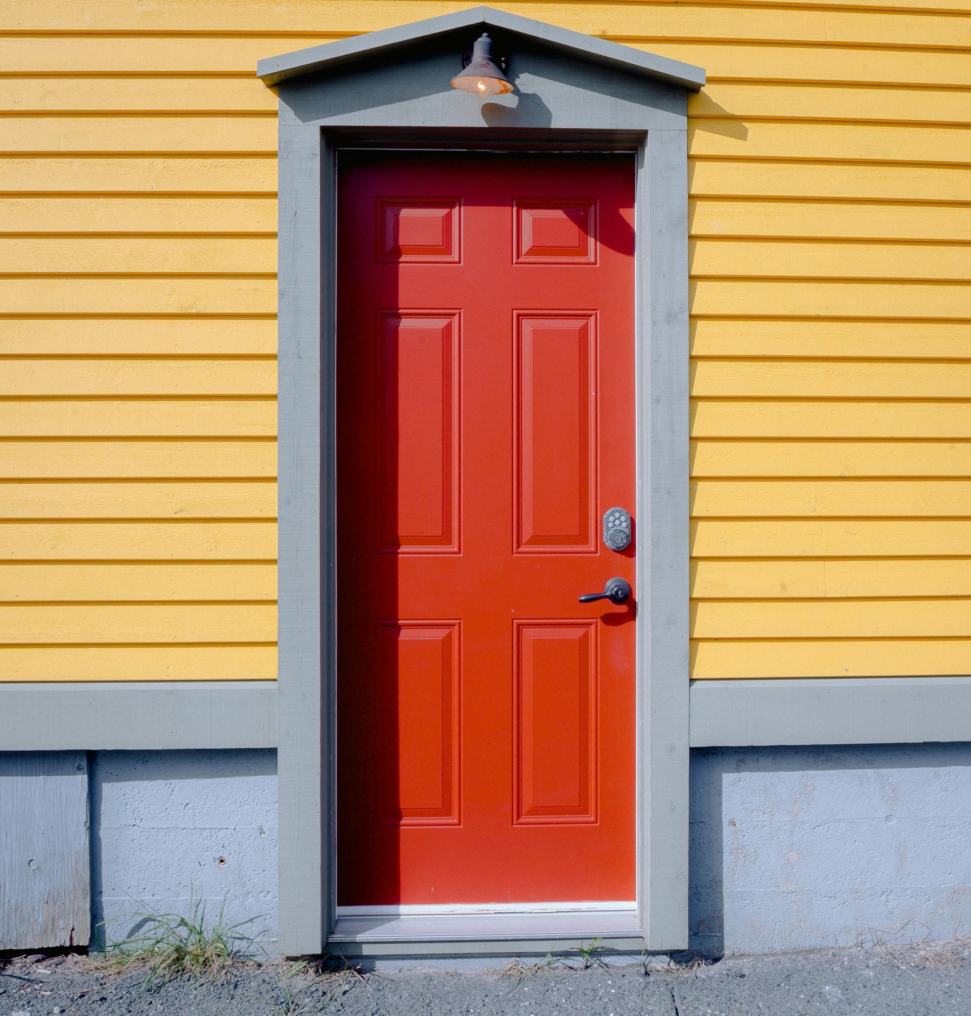 Red door centered in yellow-sided building with gray trim. A light above the door.