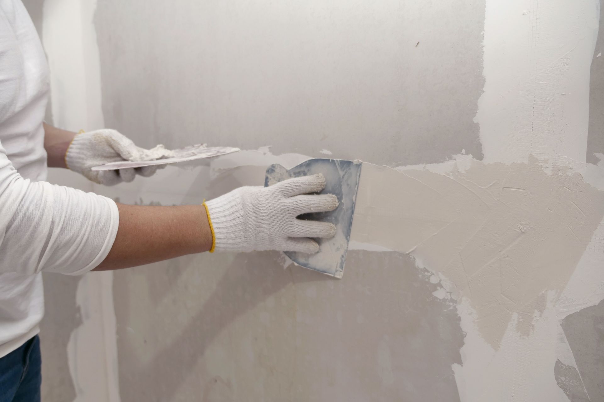 Person in white gloves, using a trowel to apply drywall compound to a wall.