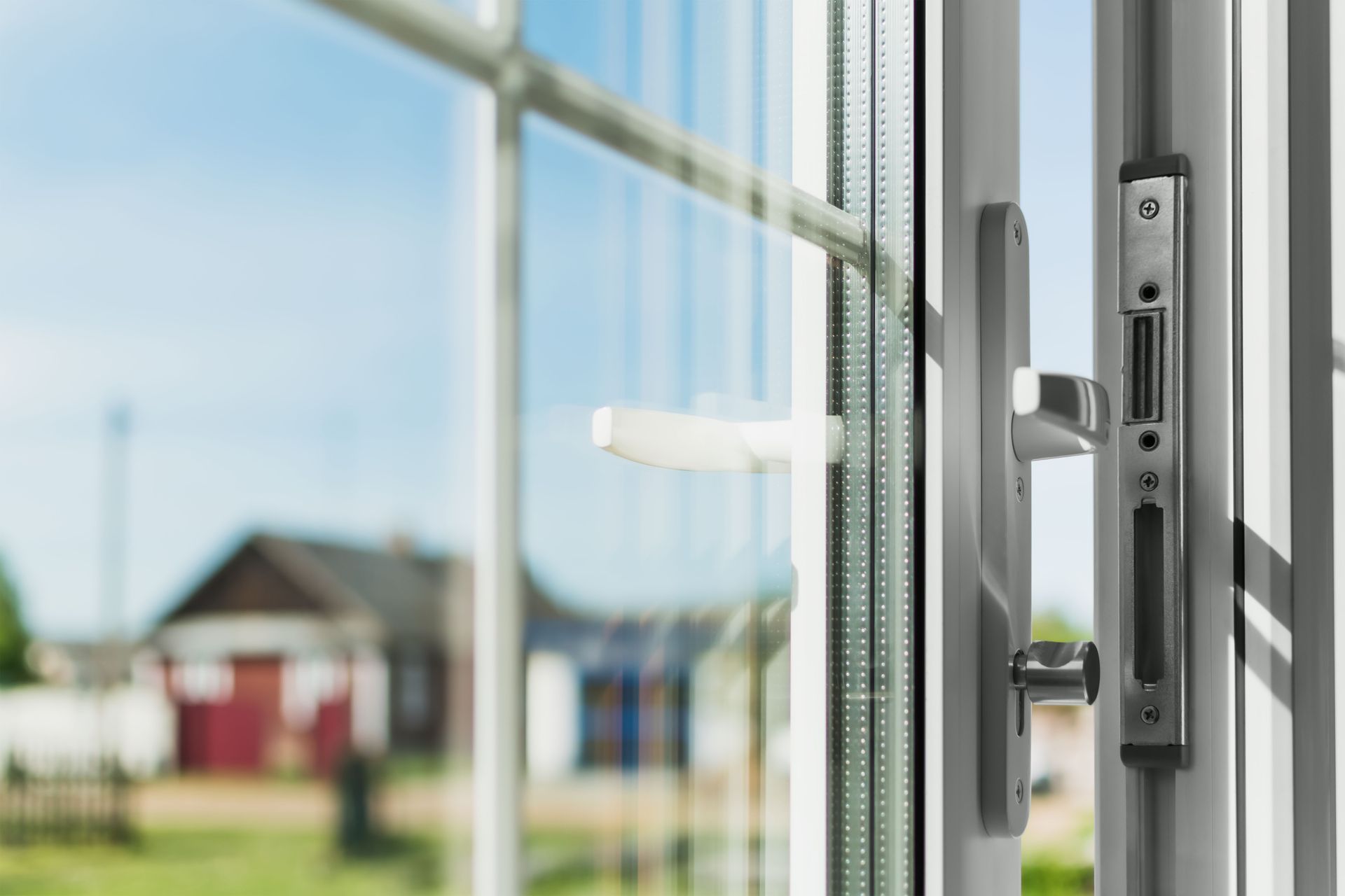 Window with a white frame and hardware open to a bright sunny day with houses visible in the distance.