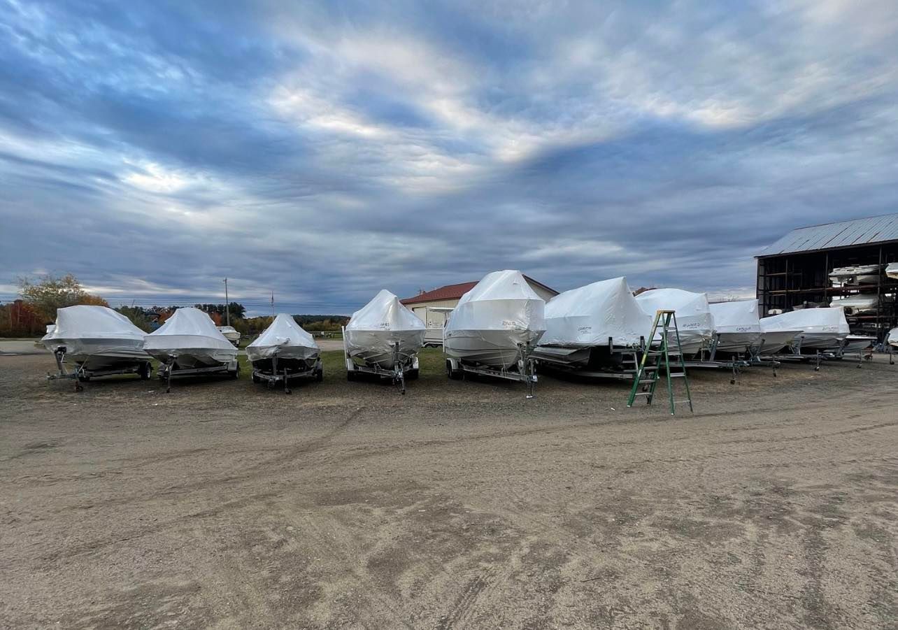 A row of boats wrapped in plastic are lined up in a parking lot.