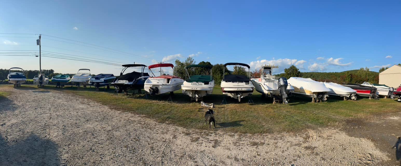 A row of boats are parked in a gravel lot.