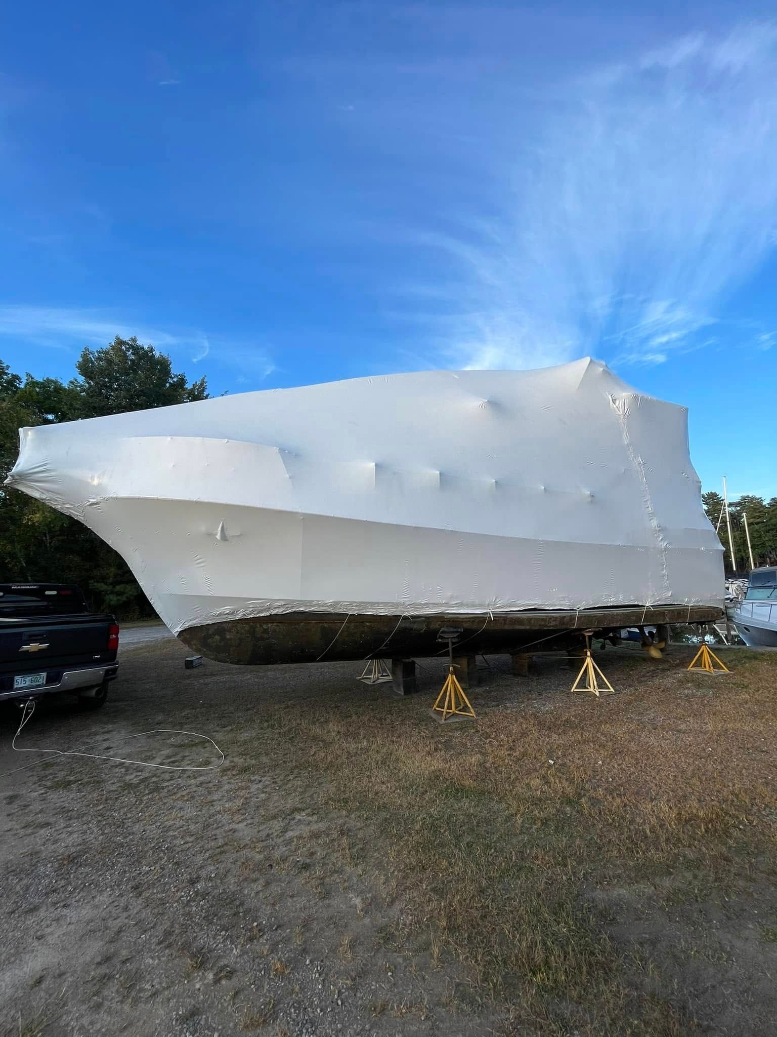 A boat wrapped in plastic is sitting in a gravel lot.