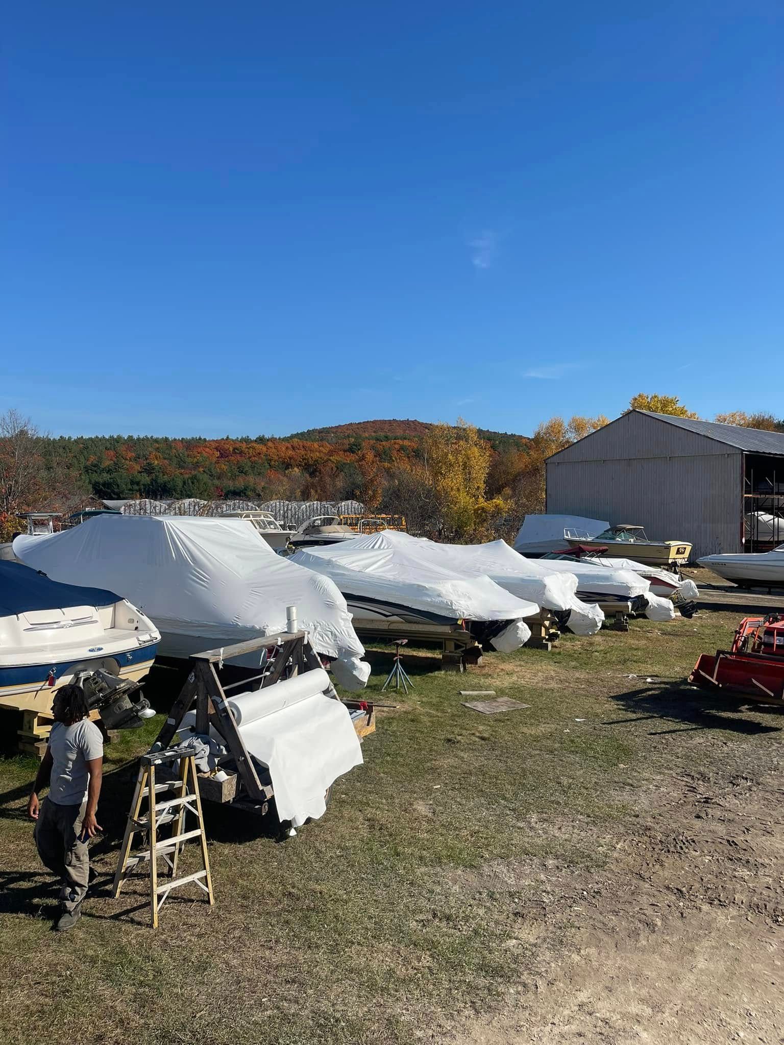 A man is standing in front of a row of boats covered in plastic.