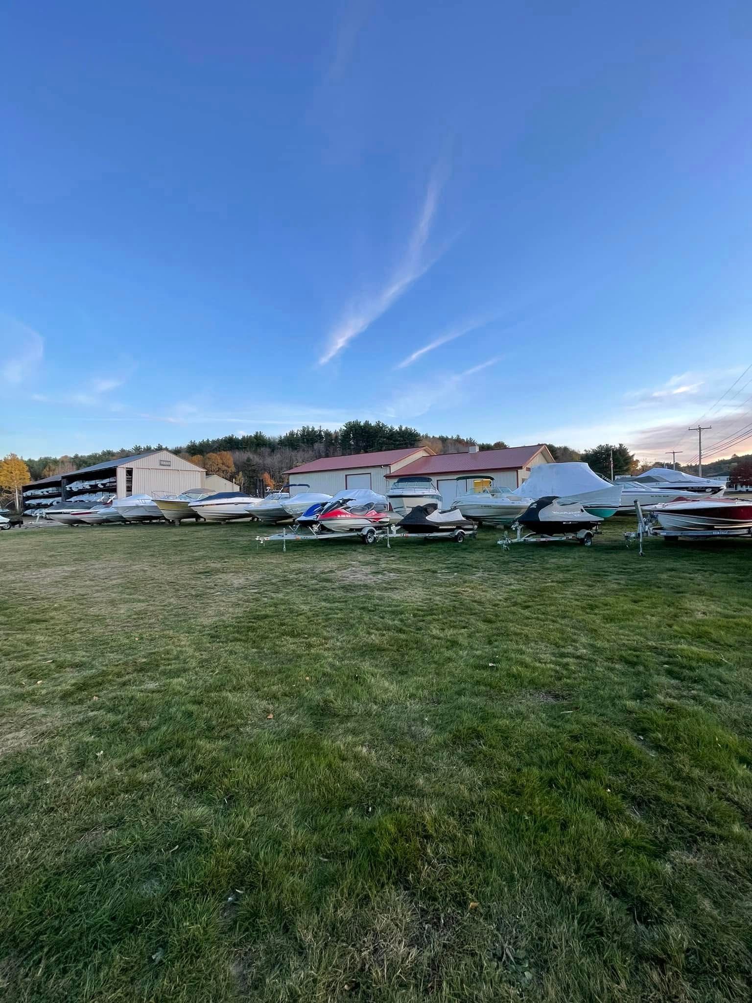 A row of boats are parked in a grassy field in front of a building.