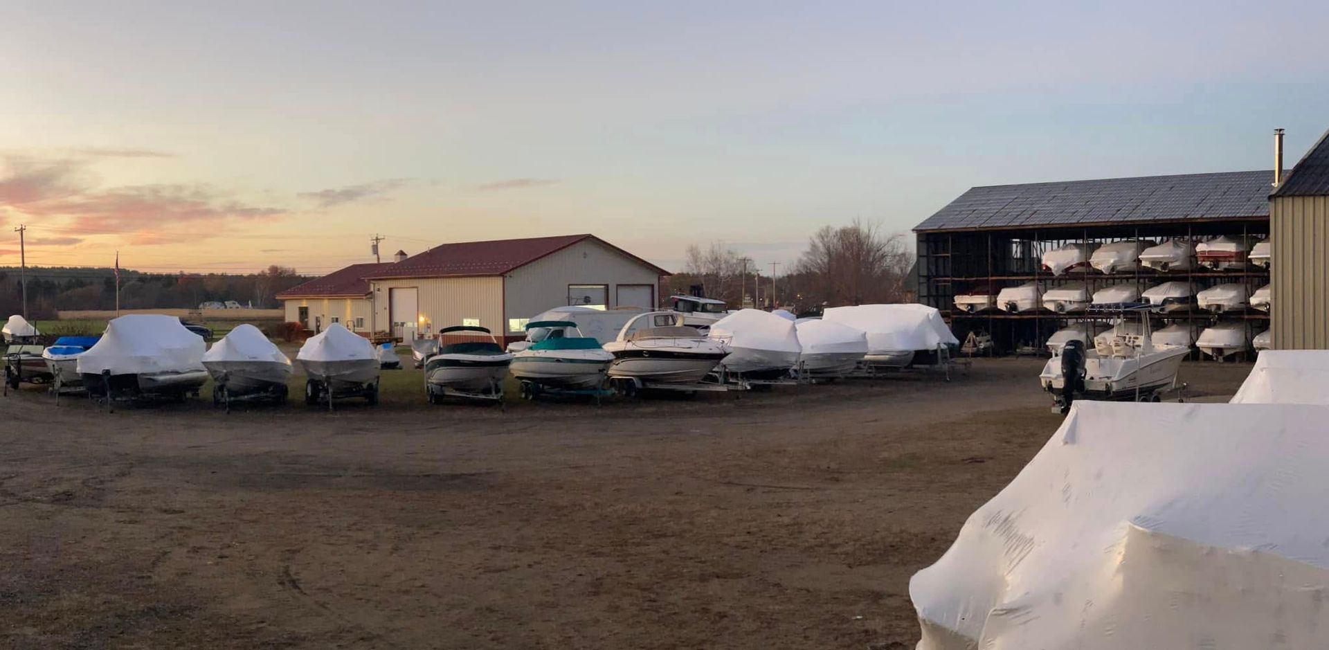 A row of boats are lined up in a parking lot covered in snow.
