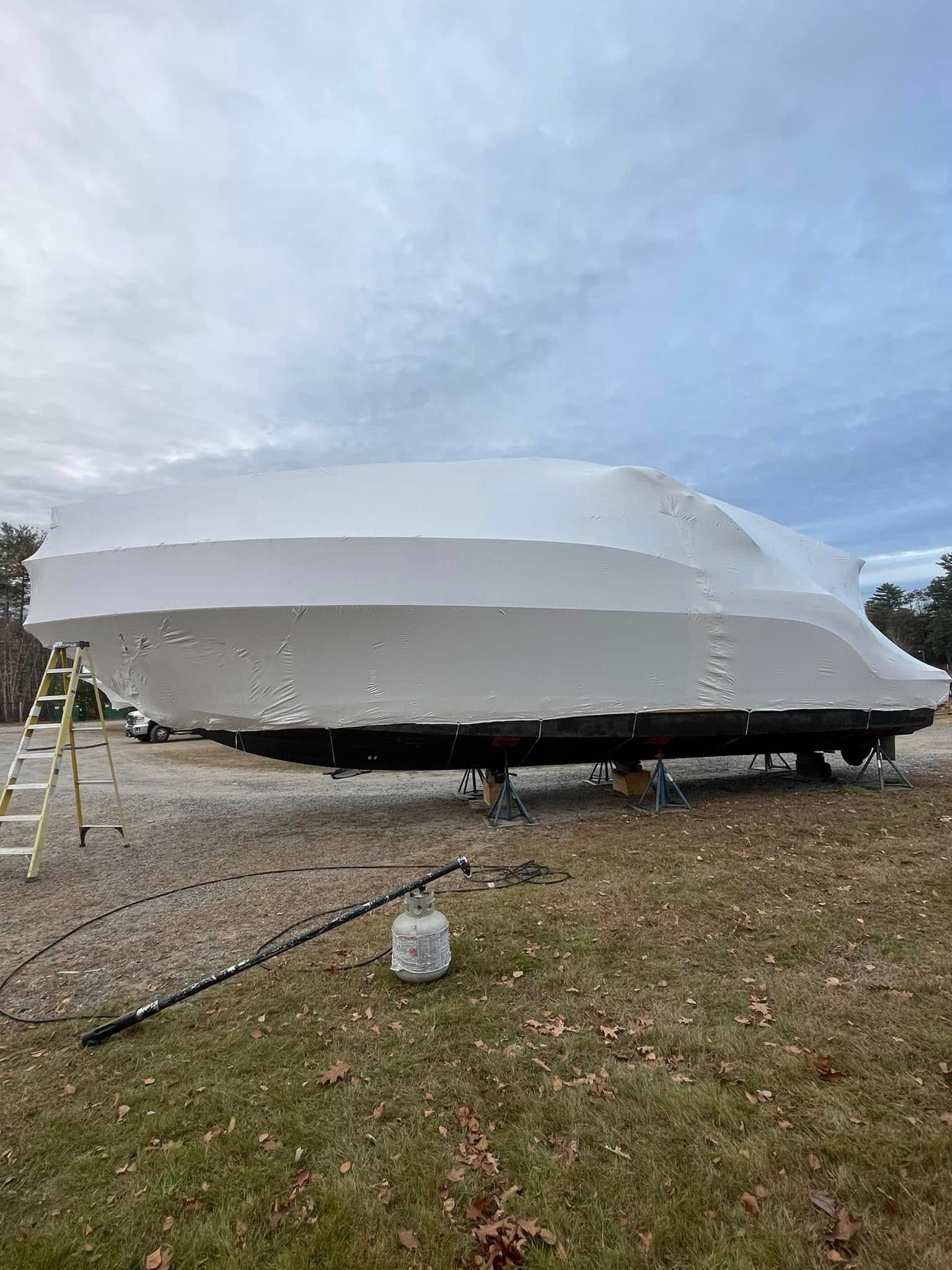 A boat is covered in a white tarp in a grassy field.