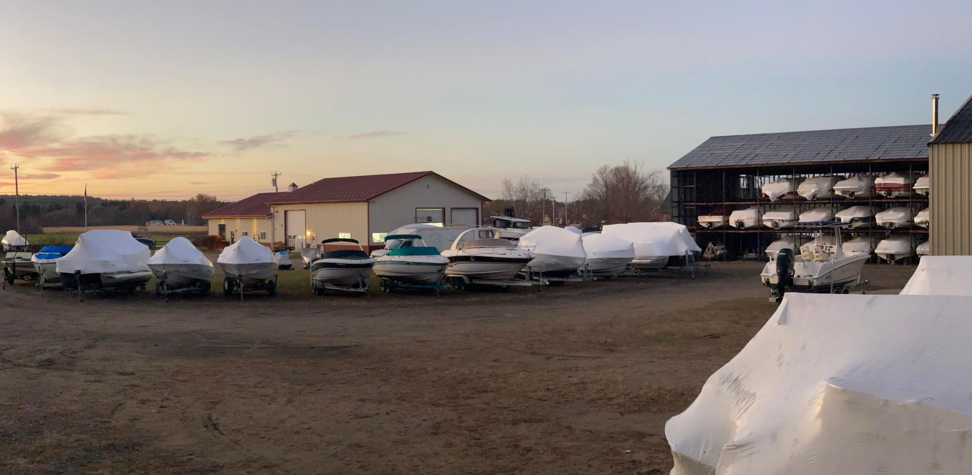 A lot of boats are covered in snow in a parking lot.