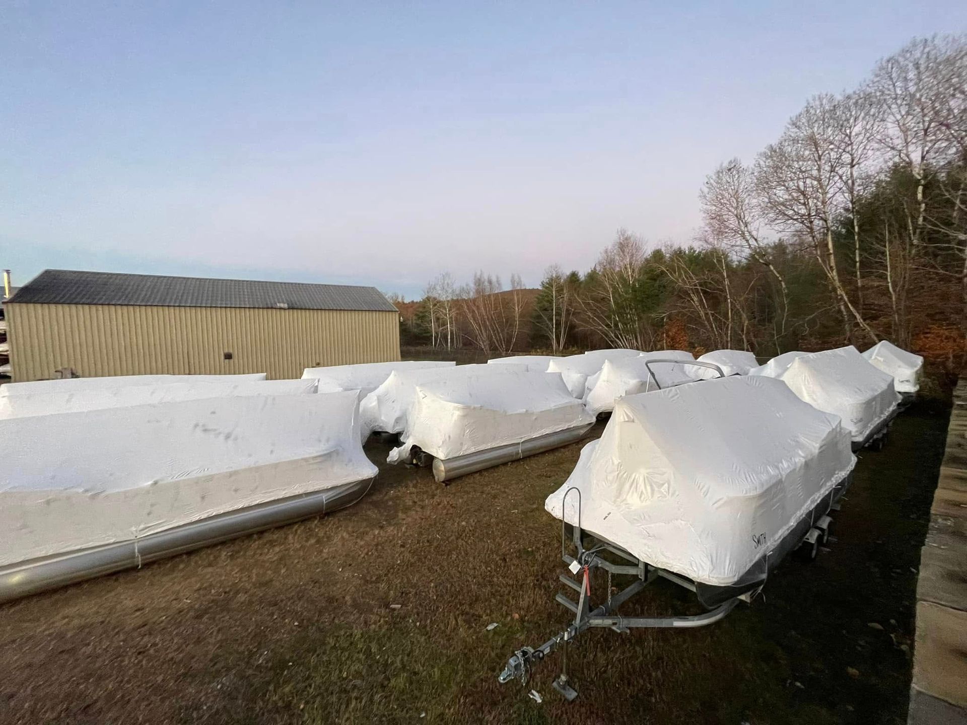 A bunch of boats are wrapped in plastic and sitting in a field.