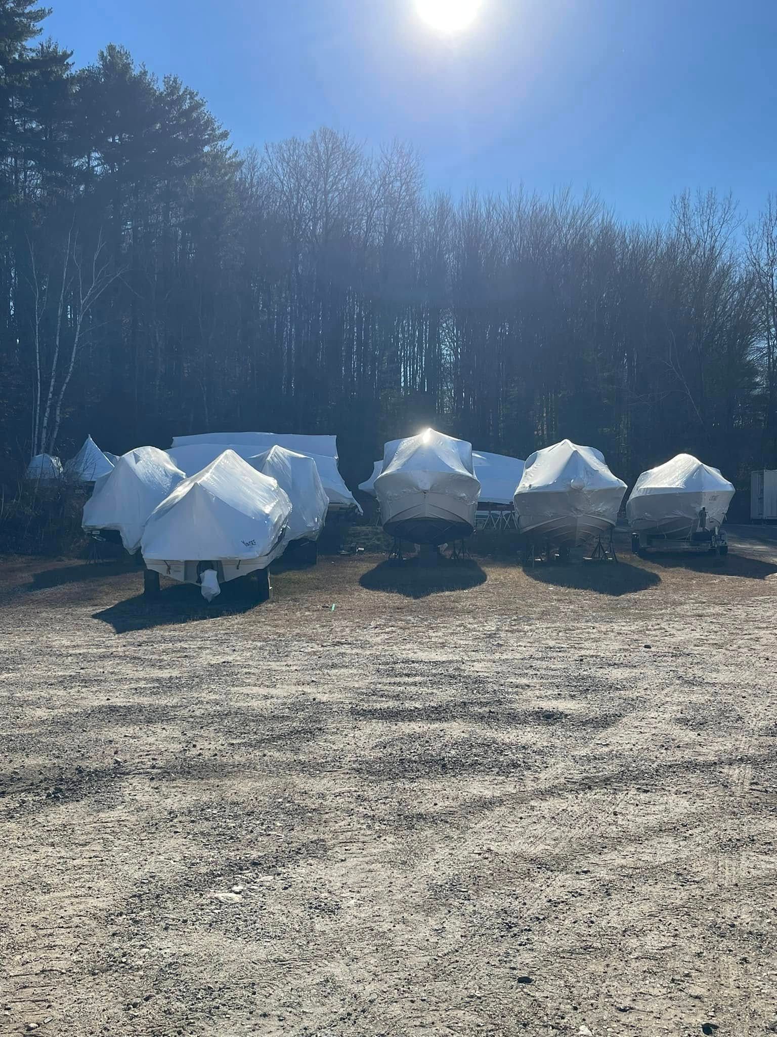 A row of boats covered in snow in a gravel lot.