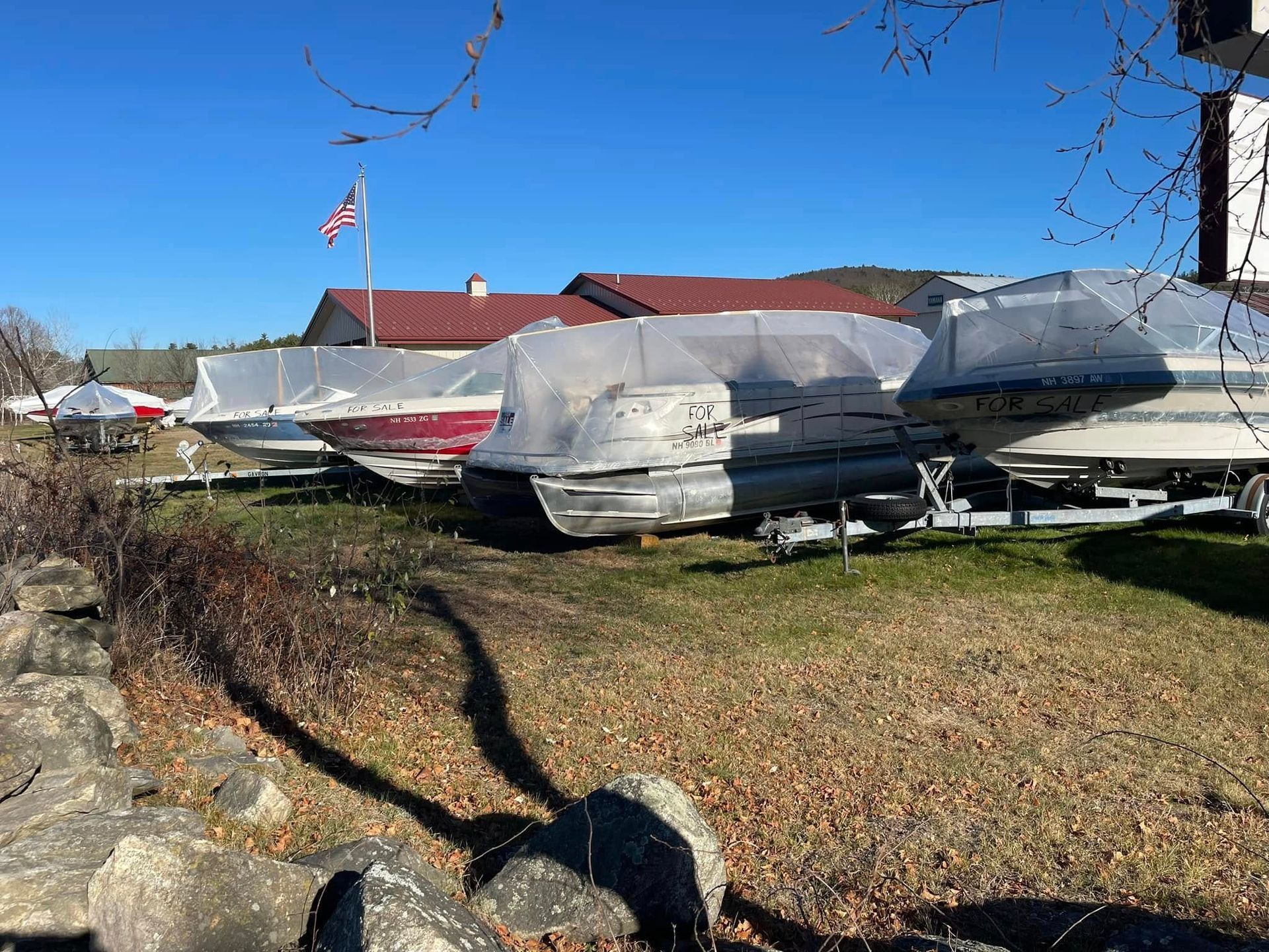 A row of boats covered in plastic are parked in a grassy field.