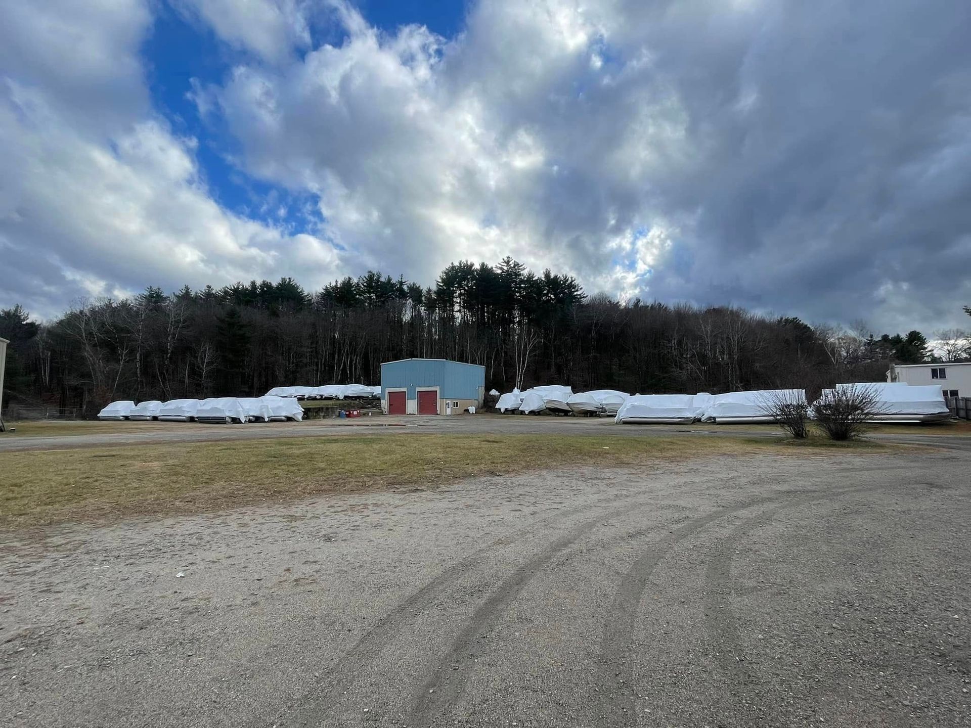 A lot of trailers are parked in a gravel lot in front of a building.