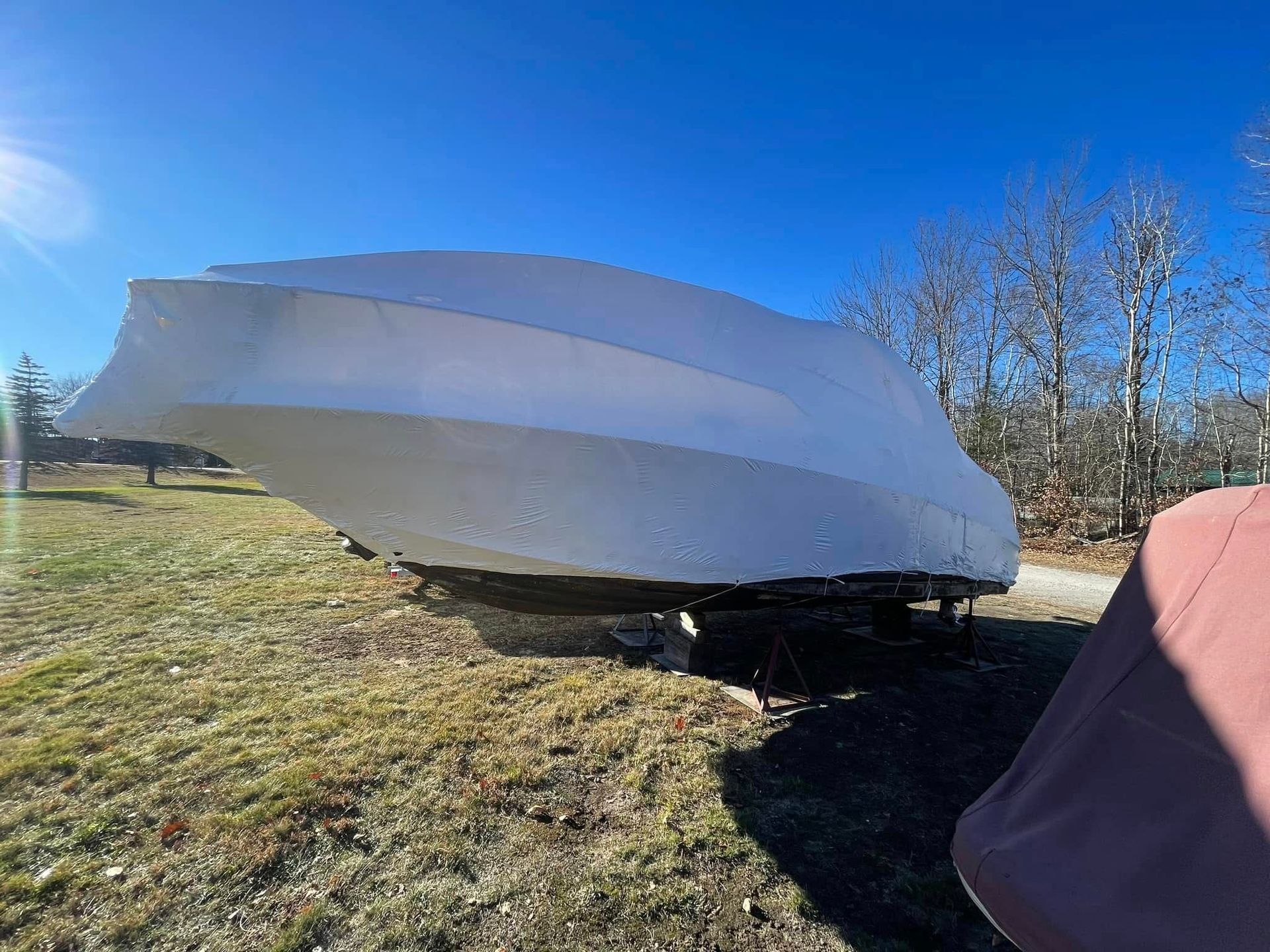 A boat is covered in a white tarp in a field.