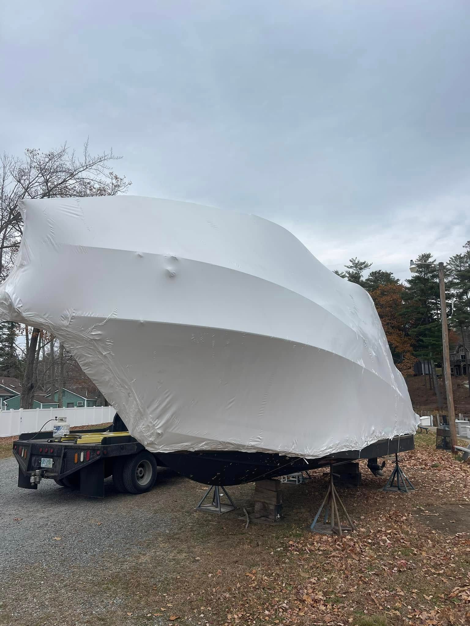 A boat is wrapped in plastic and sitting on a trailer.