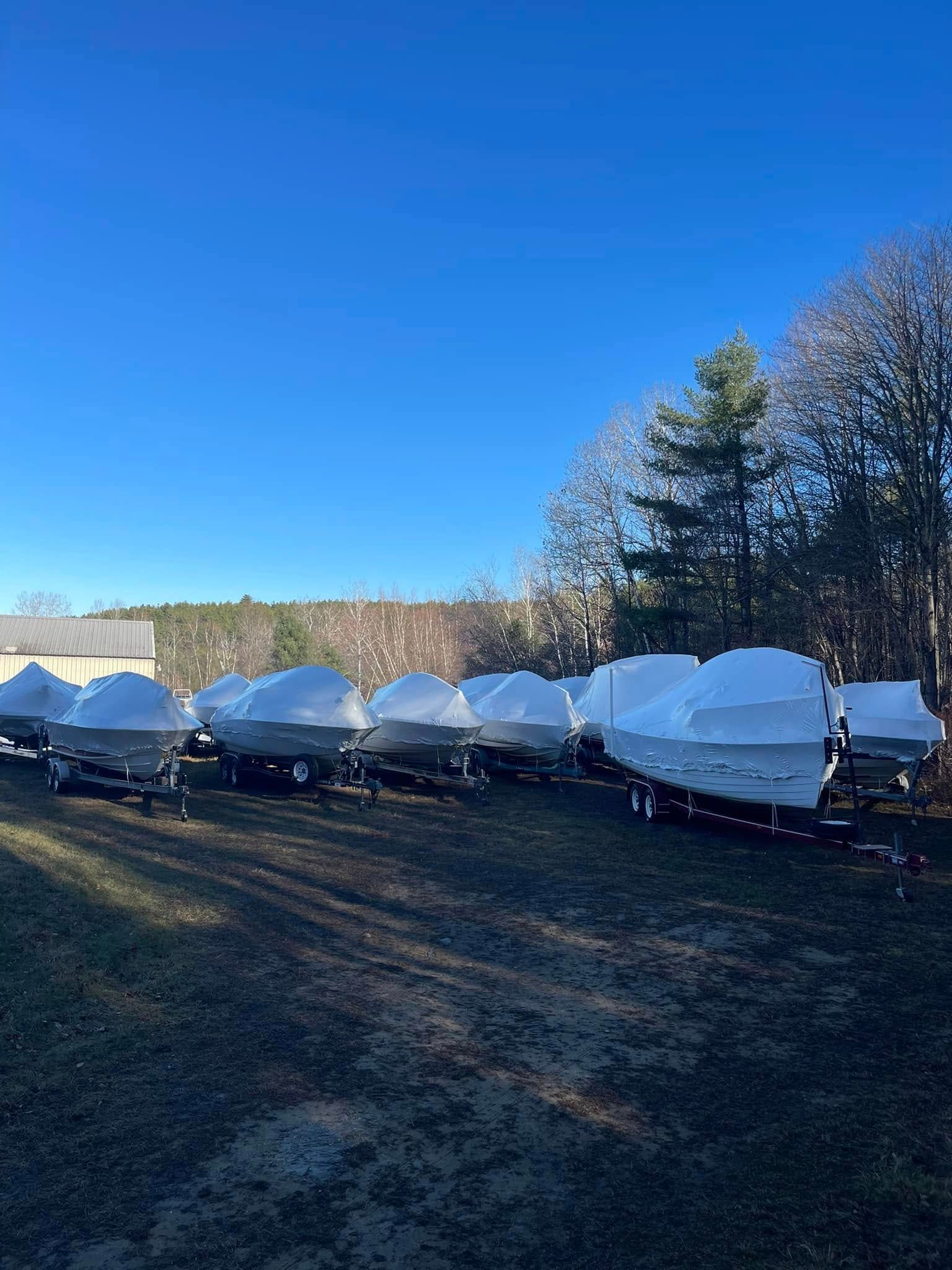 A row of boats wrapped in plastic are parked in a field.