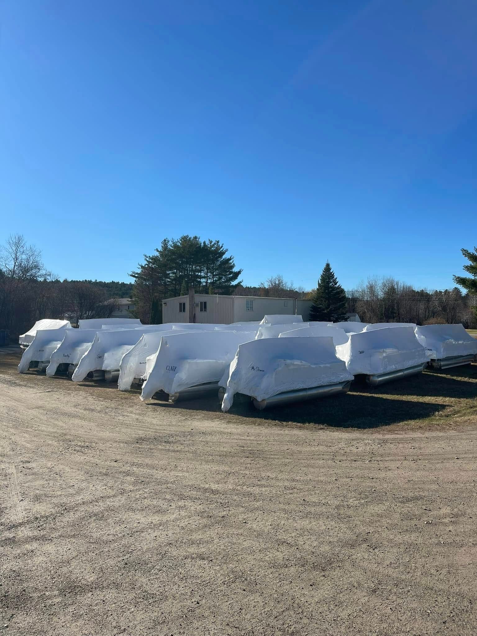 A row of white boats are lined up in a gravel lot.