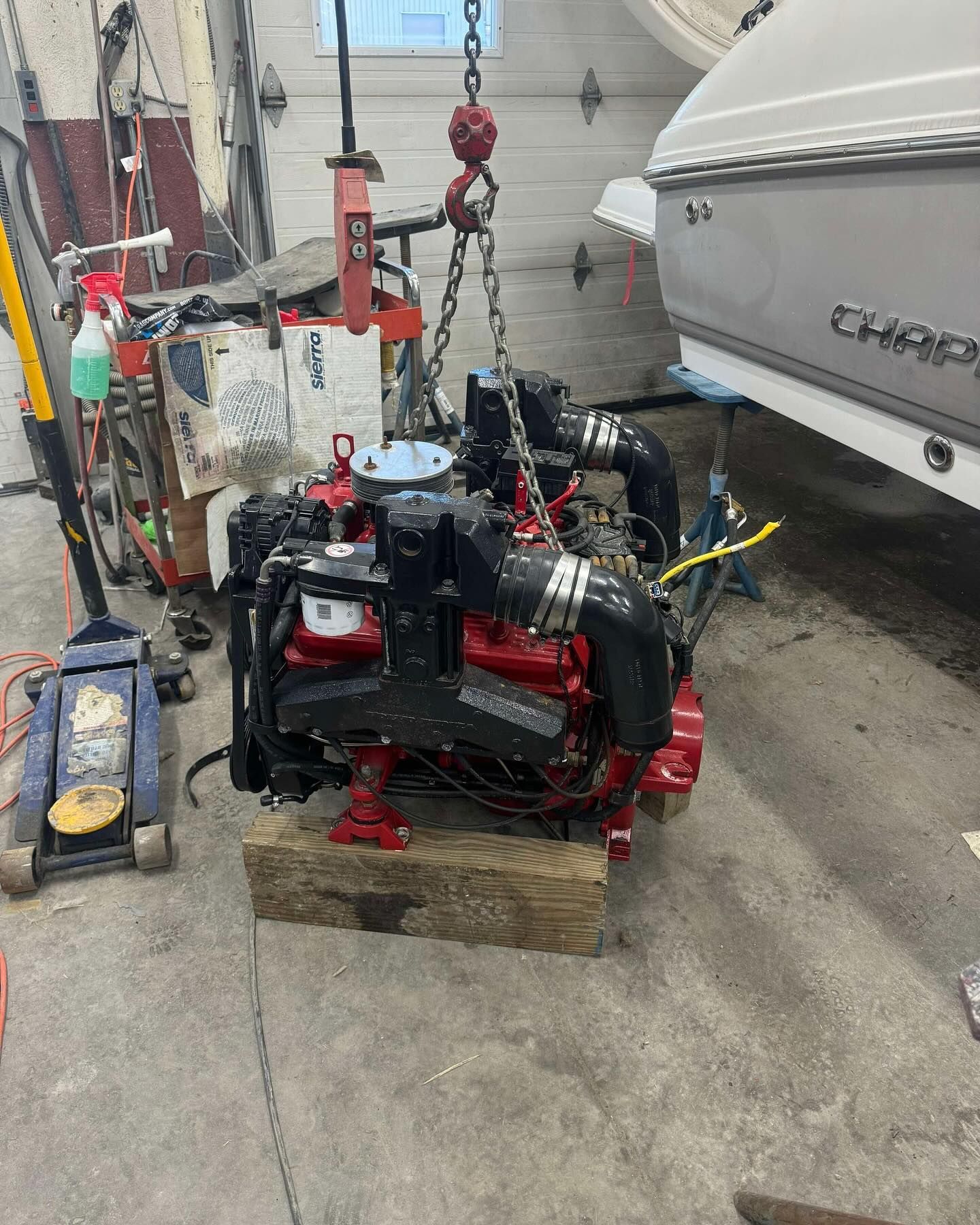 A boat engine is sitting on a wooden block in a garage next to a boat.