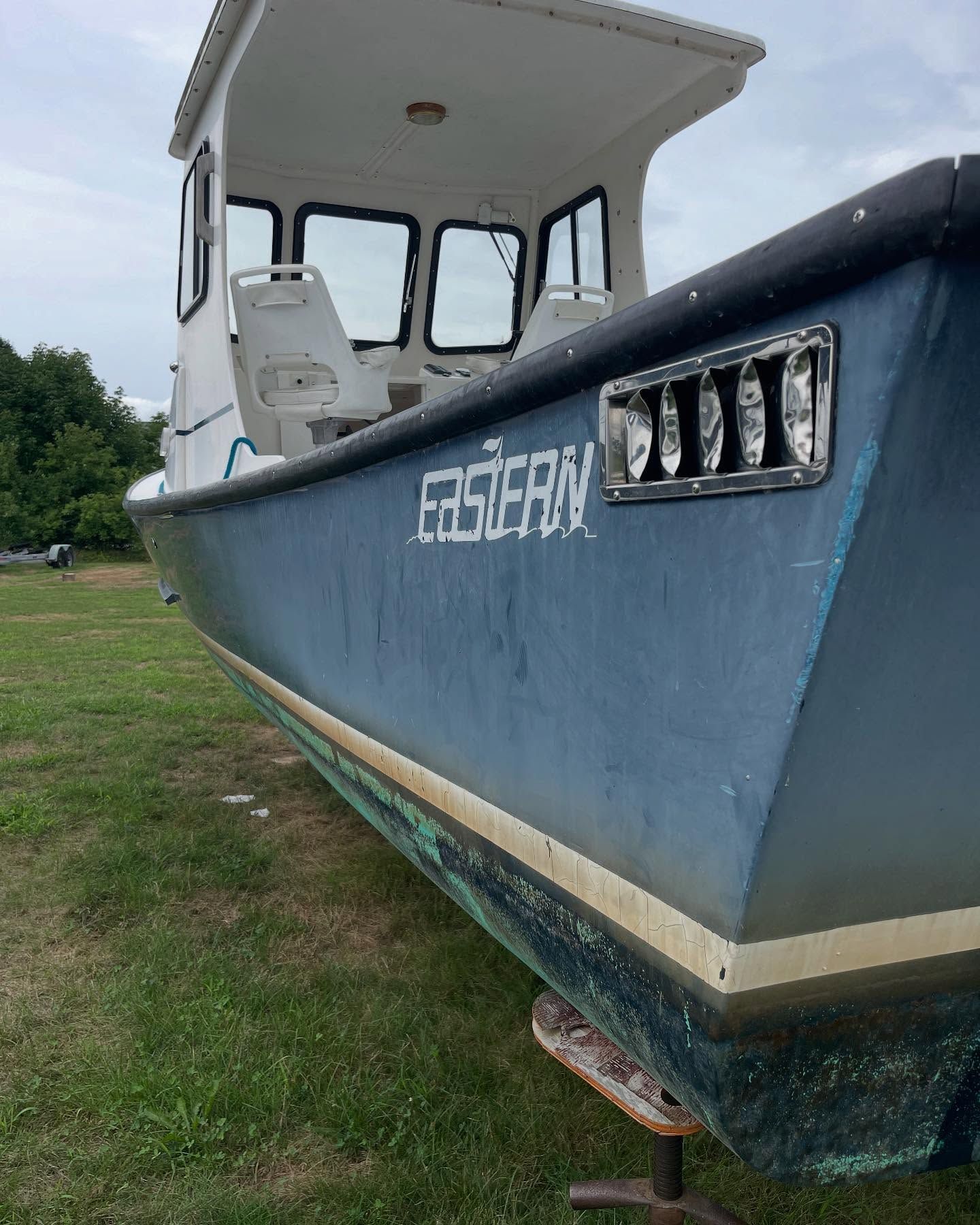 A blue boat with the name eastern on the side is parked in a grassy field.