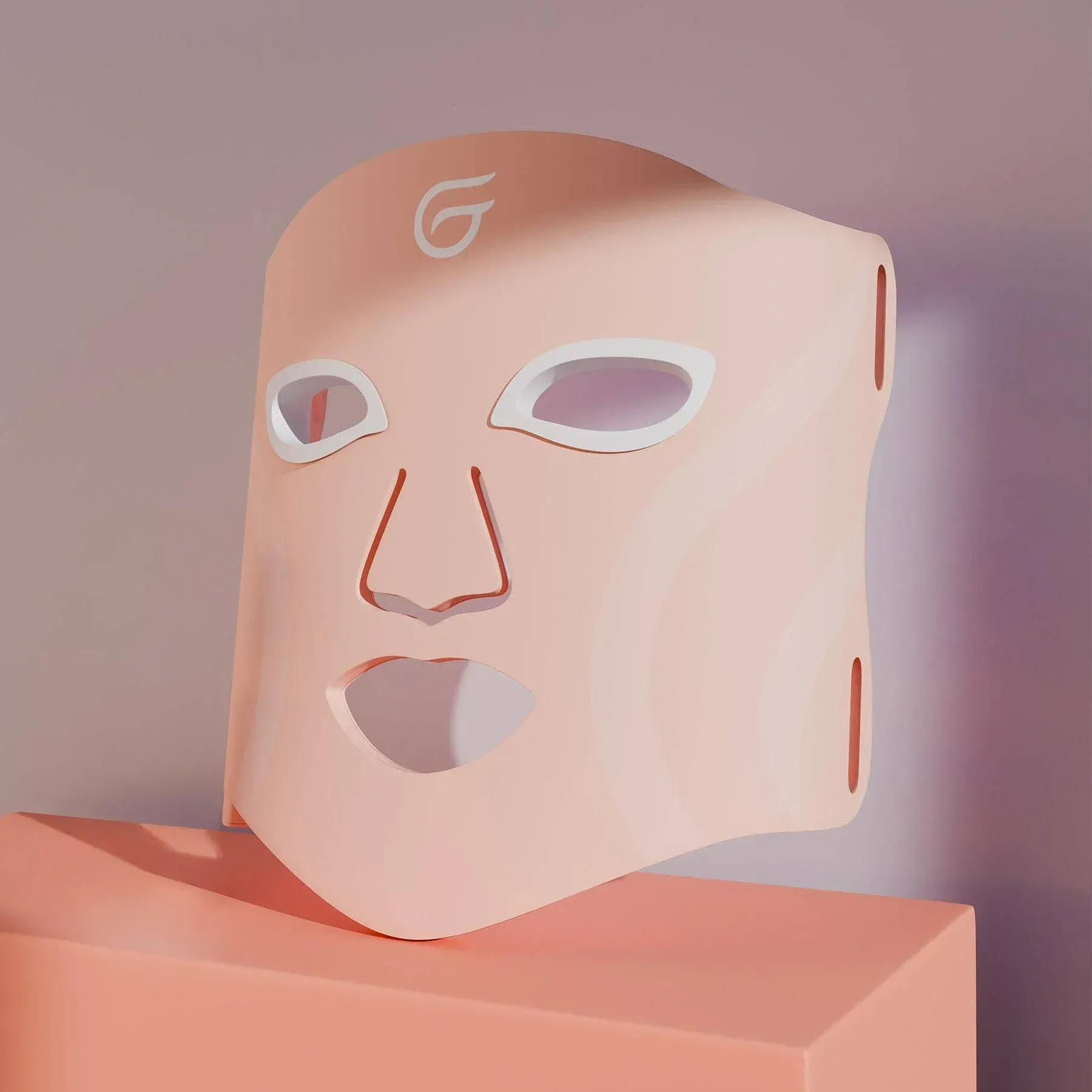 Pink LED face mask on a pink block with a soft pink and purple backdrop.