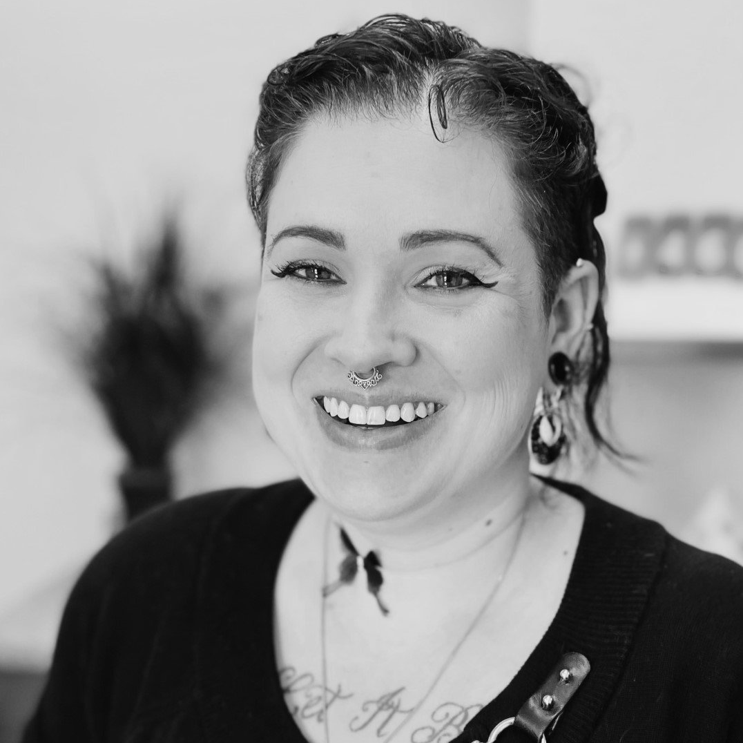 Woman with septum piercing, smiling, wearing earrings, black top.